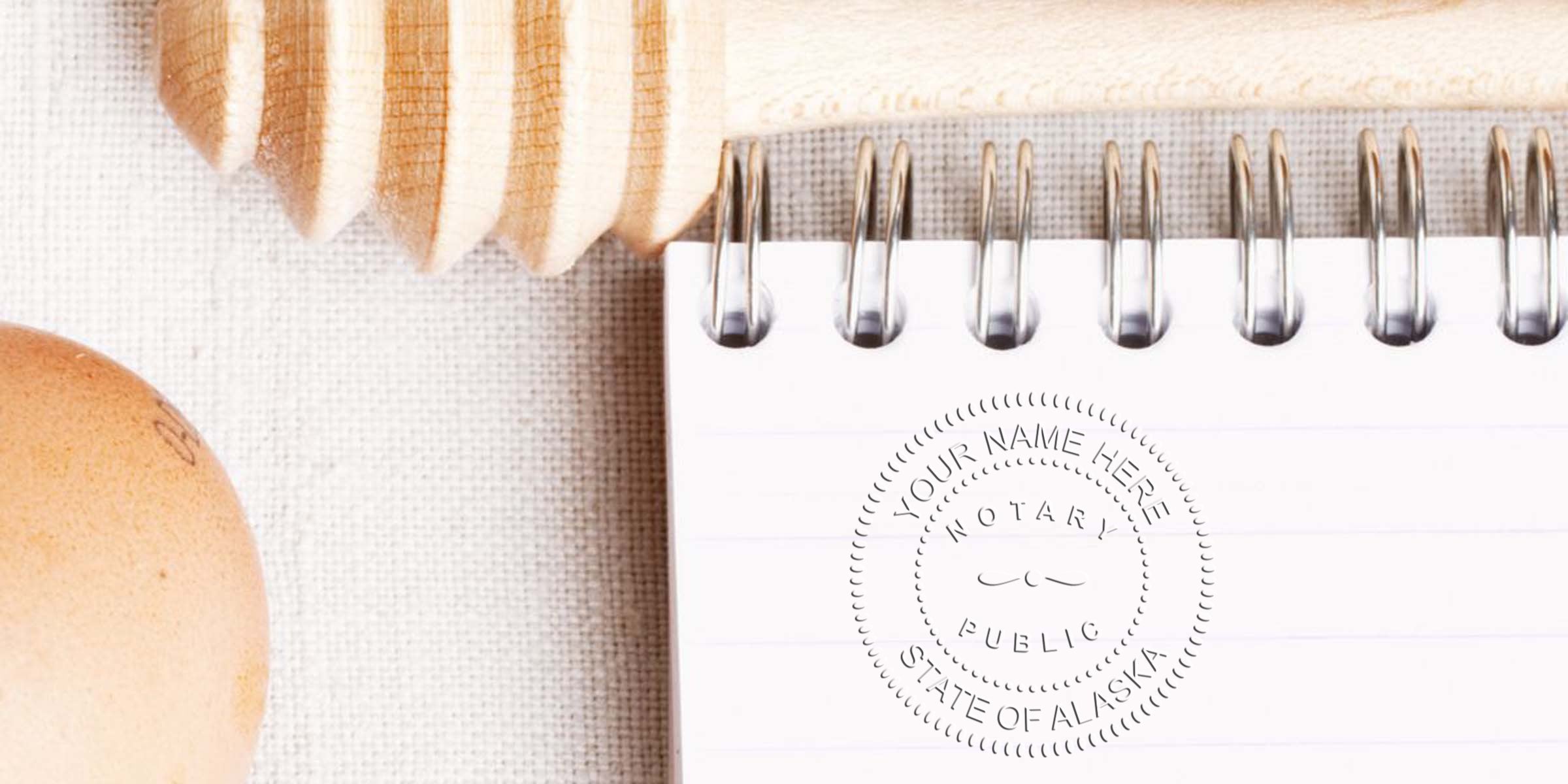 AK notary seal on white spiral notebook with wooden honey dipper and egg on linen background, showing a notary seal checklist.