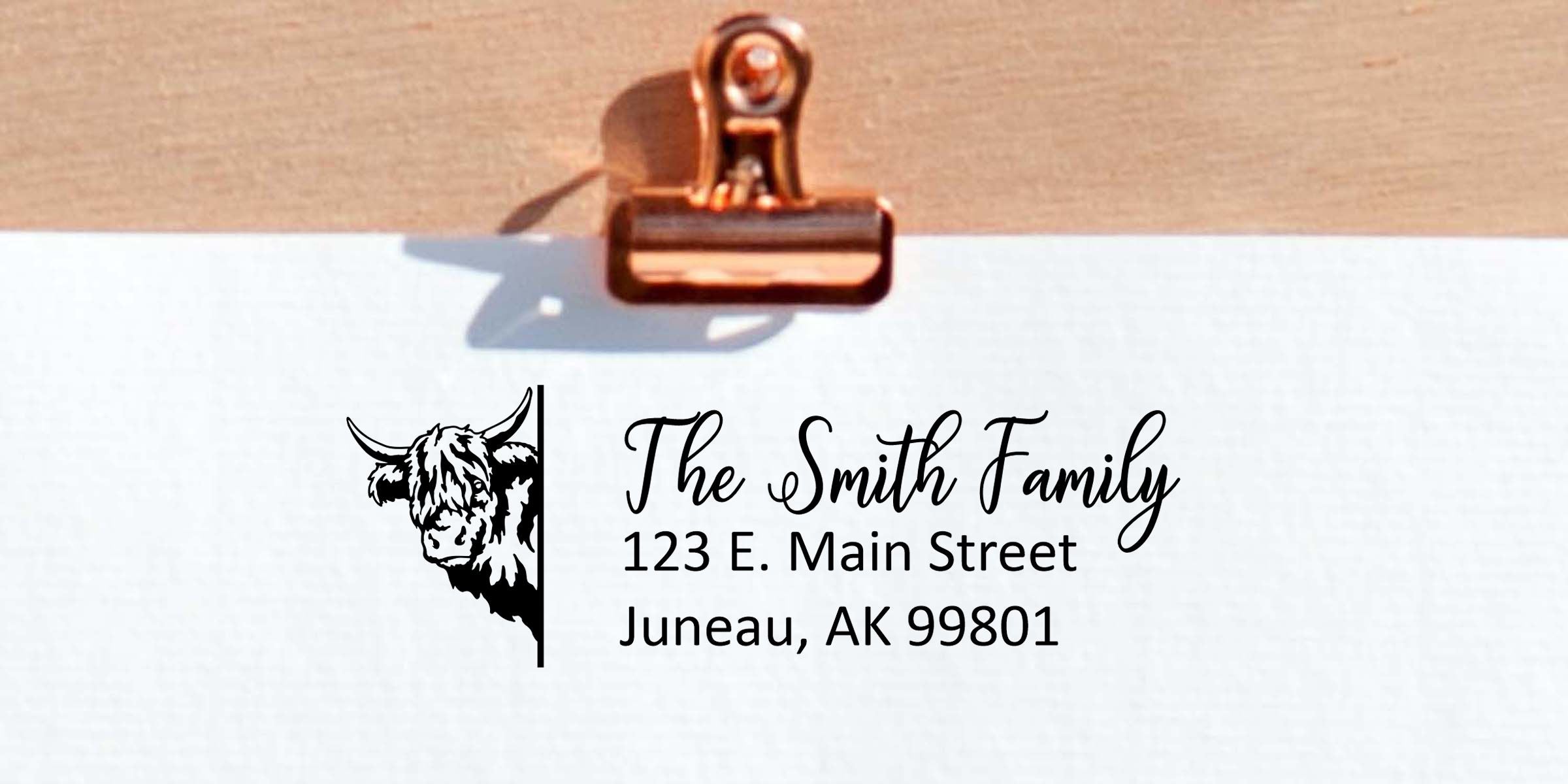 Personalized address label with cow logo, “The Smith Family,” 123 E. Main Street, Juneau, AK 99801 clipped to a clipboard, custom family mailing label design
