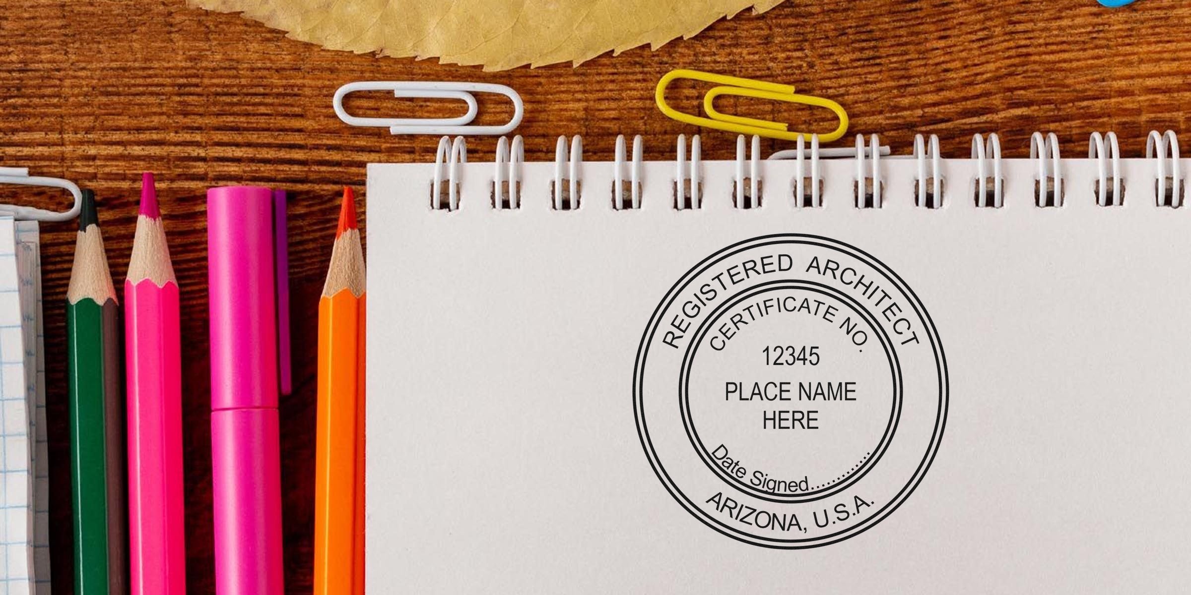 Arizona architect embosser stamp on a spiral notebook with colored pencils and paper clips on a wooden desk, showcasing custom architectural embossing and architect certification in Arizona, USA.
