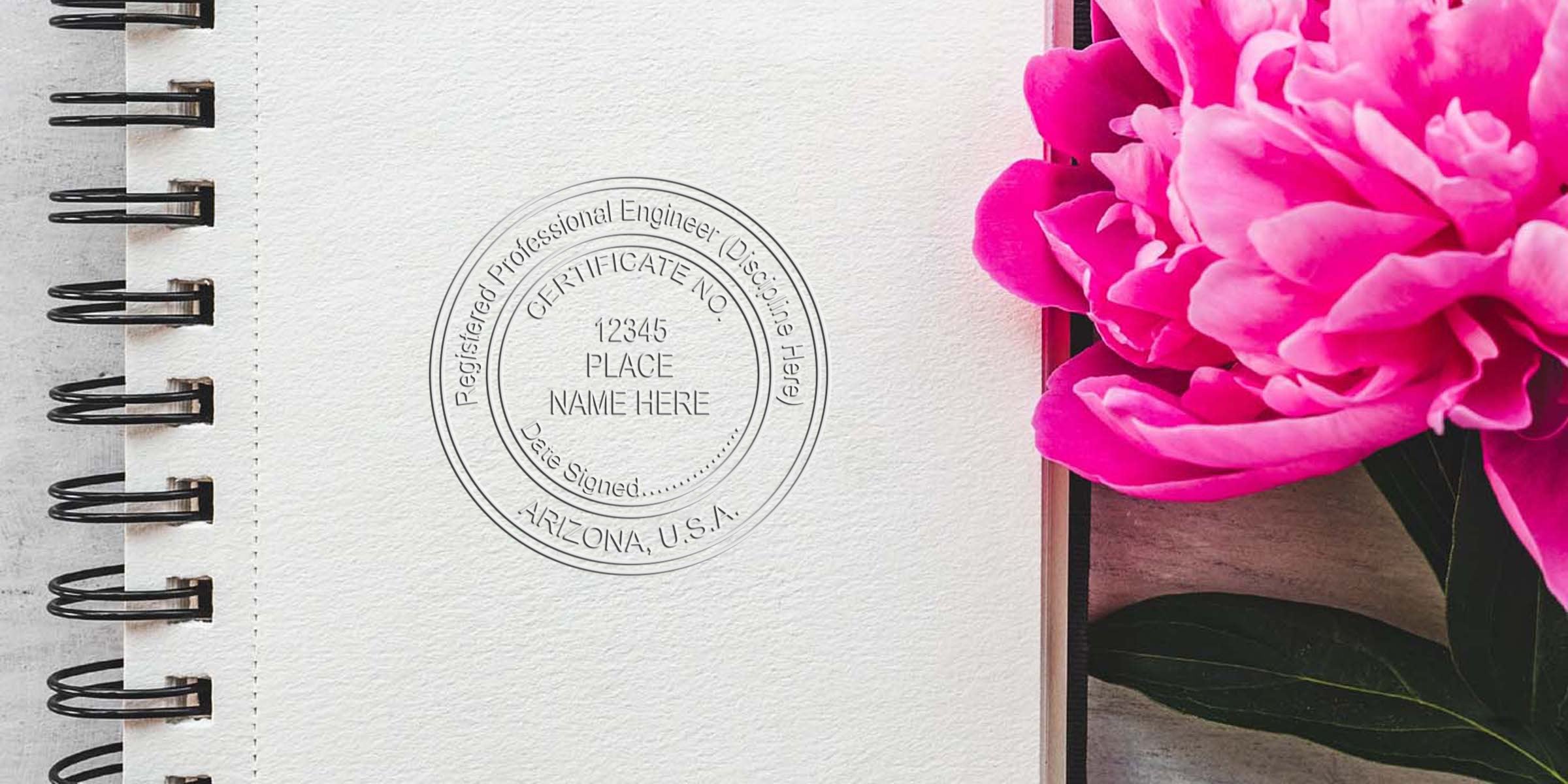 Pink peony next to a spiral notebook with a professional Arizona engineer stamp on white paper, emphasizing Arizona engineer stamp regulations.