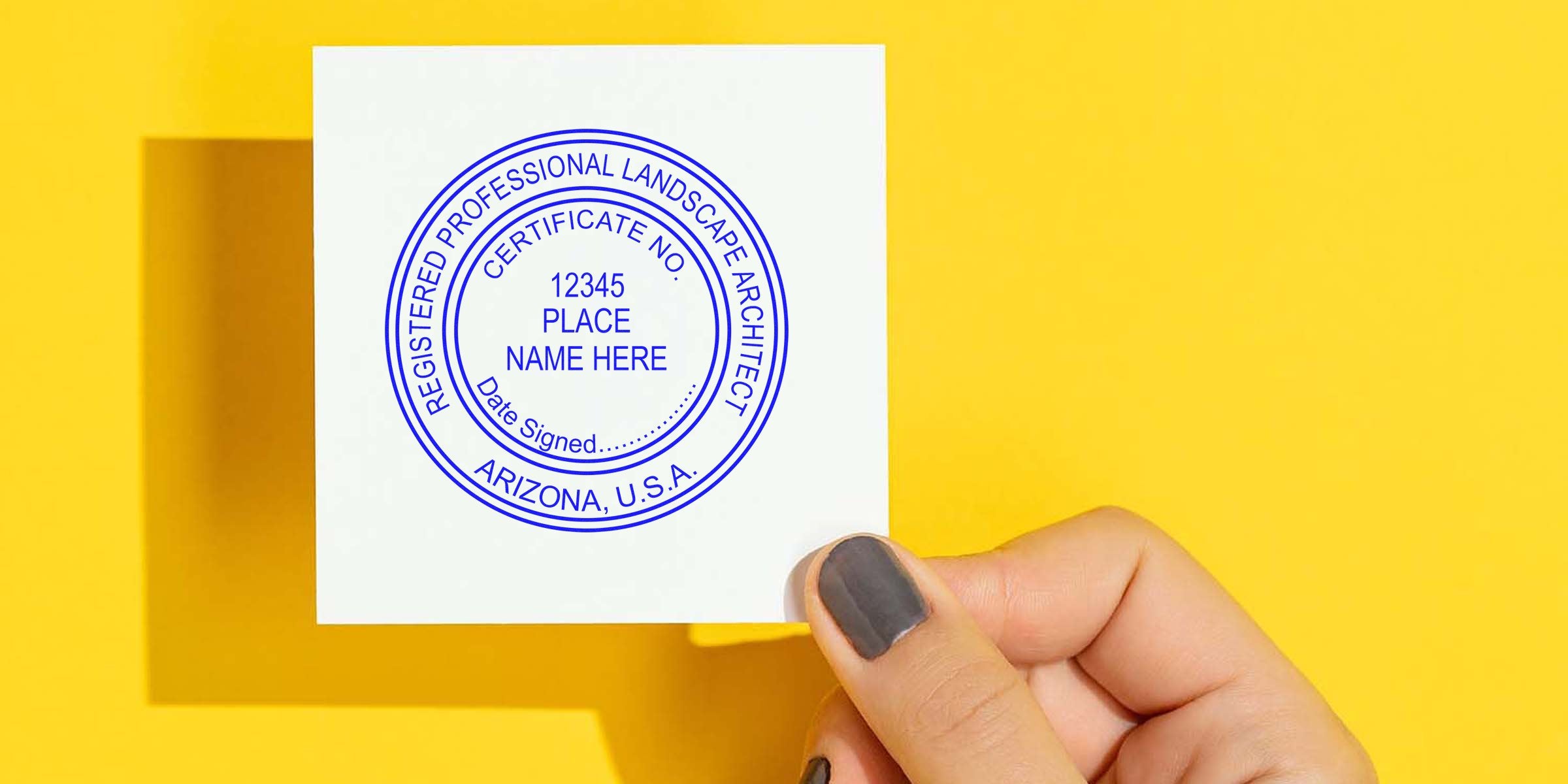 Hand holding a Landscape Architect Stamp on a registered professional certificate, meeting Arizona regulations, on white paper with a yellow background.