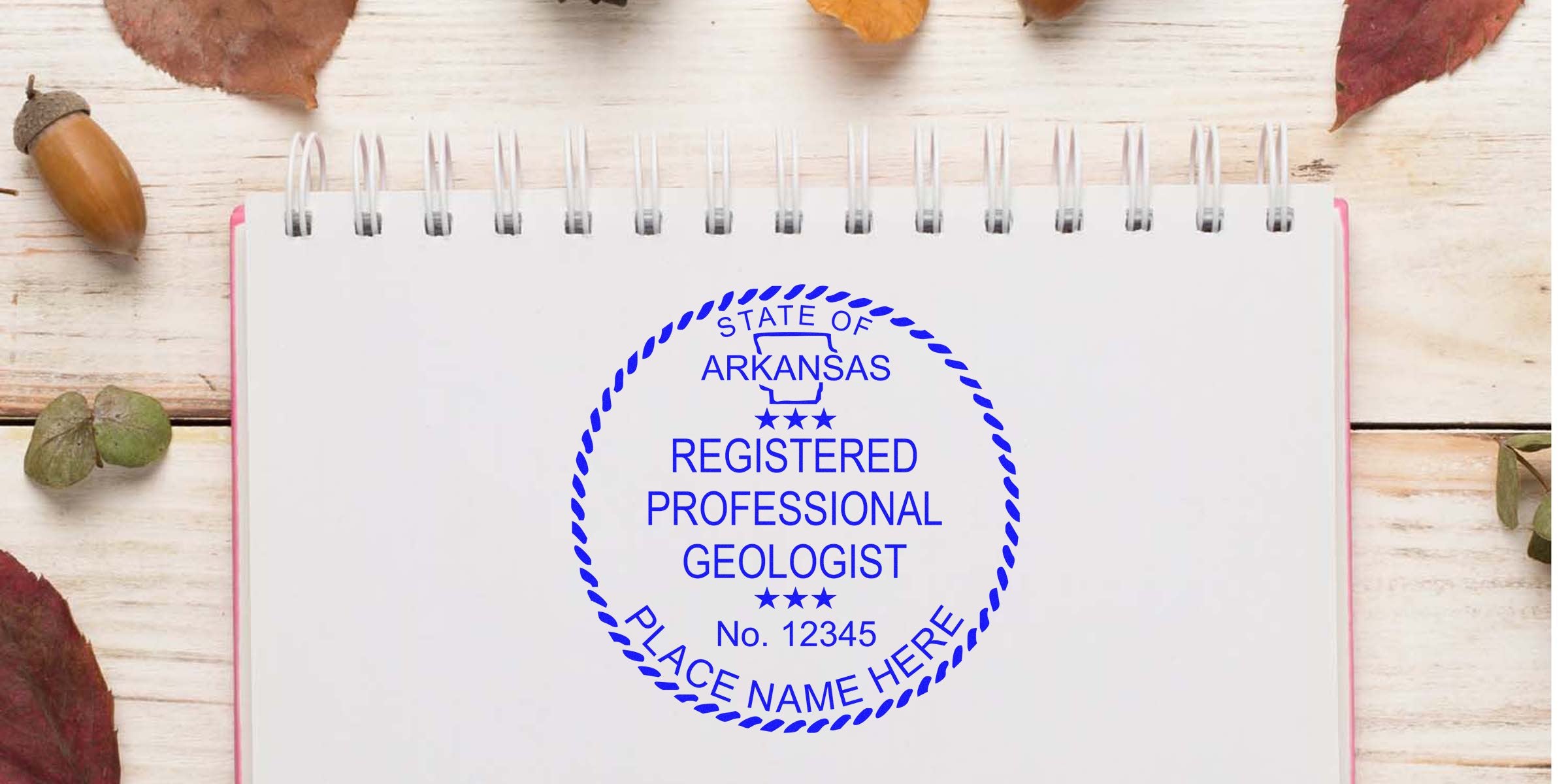 Registered professional geologist stamp on notebook with autumn leaves and acorns on wooden table, showing Arkansas geologist stamp rules and regulations.