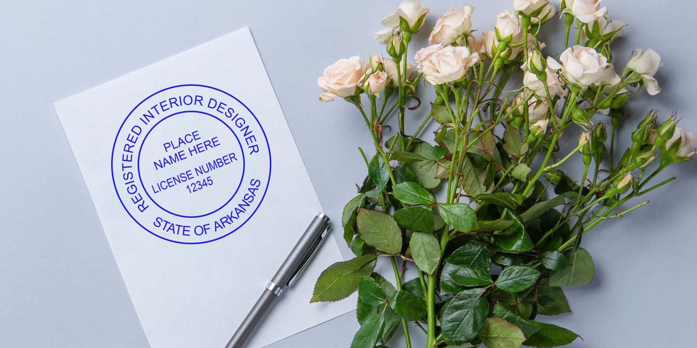 Arkansas interior designer license stamp on paper with a pen and white rose bouquet, displaying stamp details.