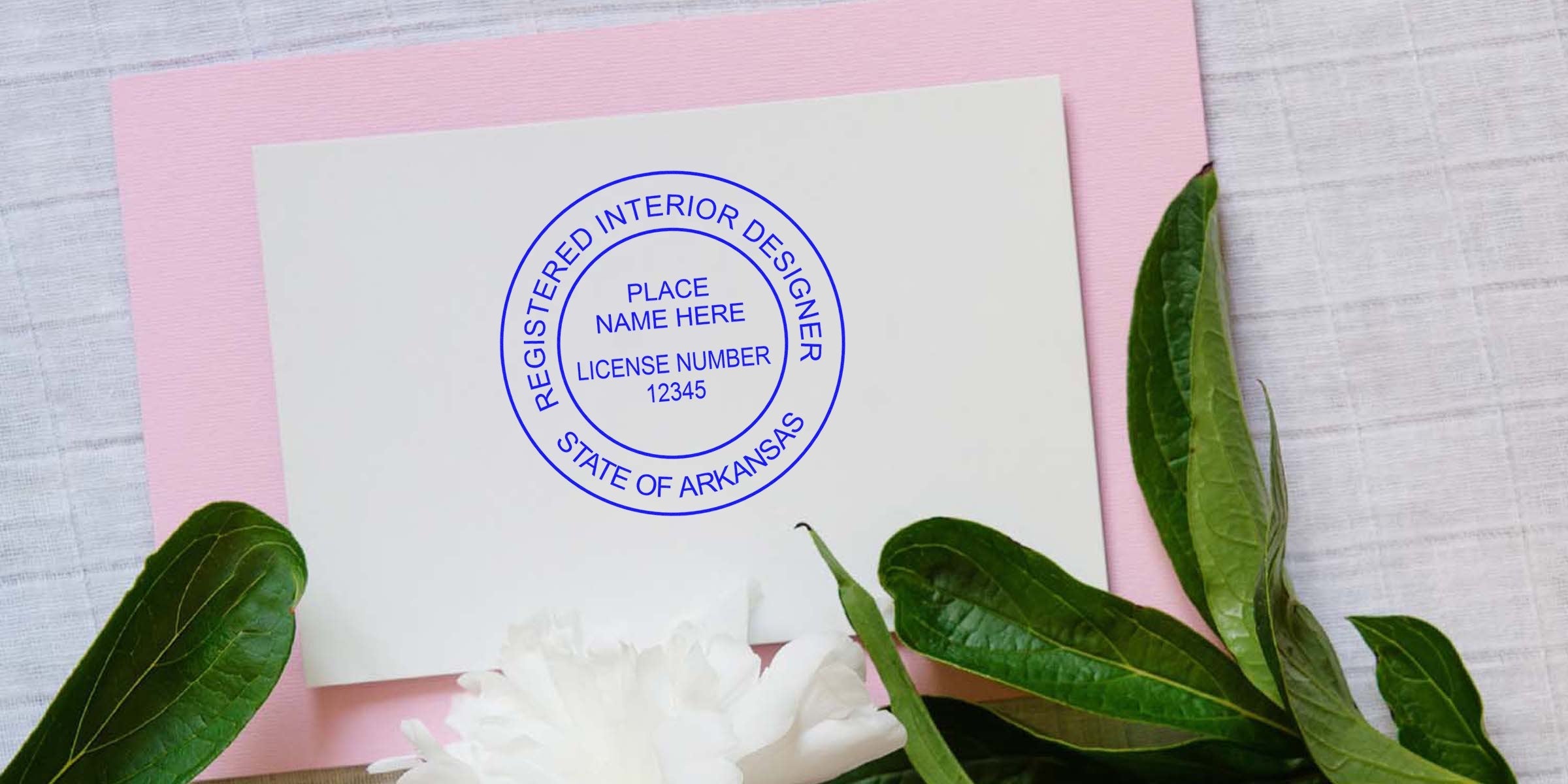 Arkansas interior designer certification seal and license number on white card with green leaves and white flower against pink and white background, highlighting interior designer stamp requirements.