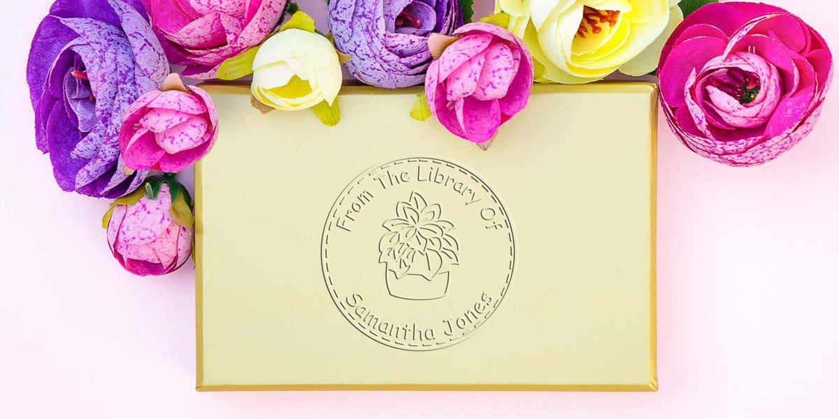 Personalized yellow gift box with colorful artificial flowers and embossed “From the Library of Samantha Jones” logo on a pastel pink background