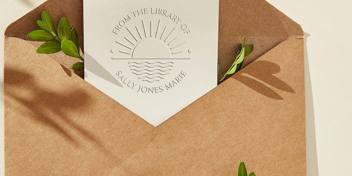 Brown kraft envelope with white embossed invitation card featuring a sunrise logo and the name Sally Jones Marie, accented with green leaves and soft natural light.