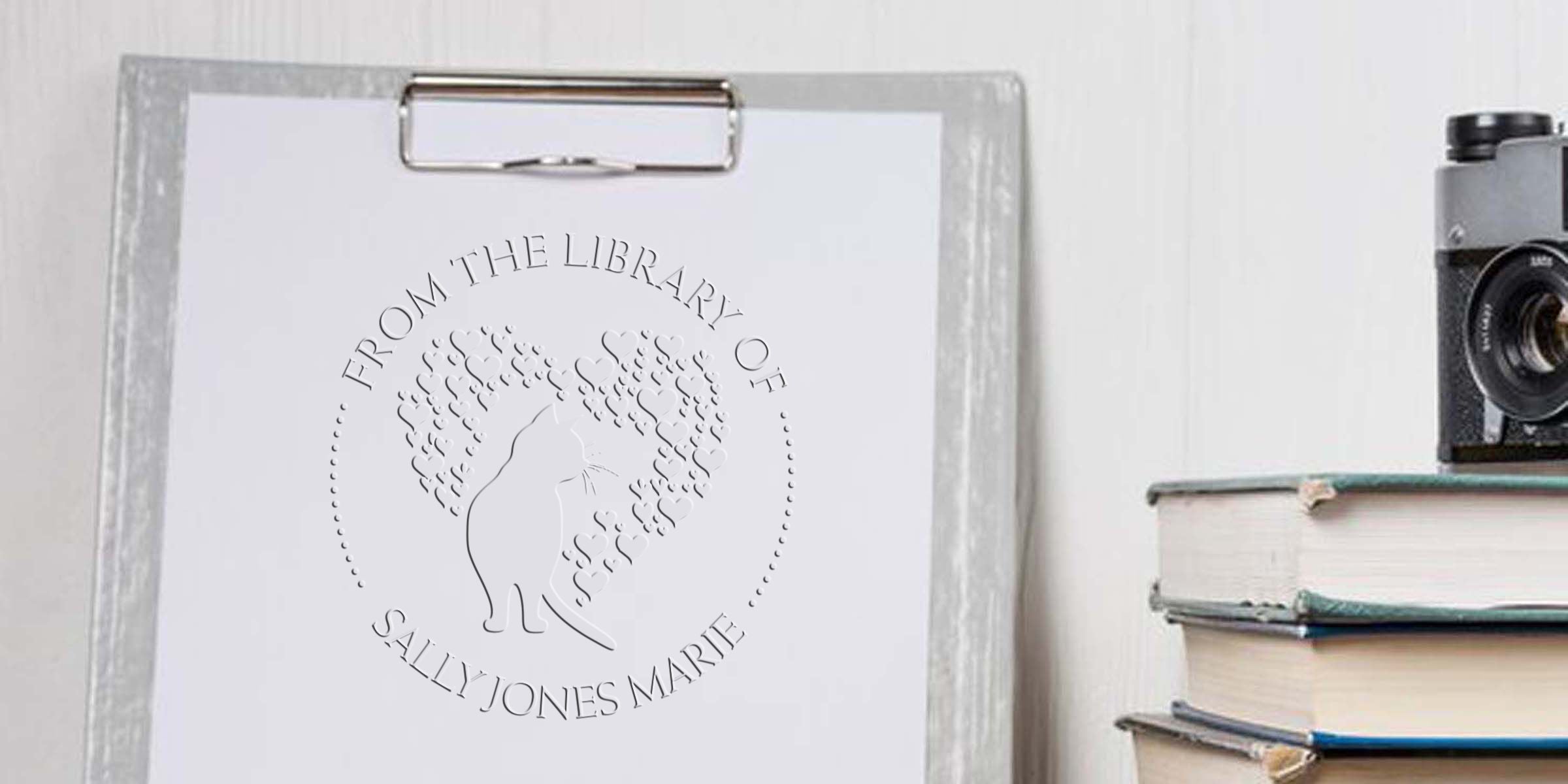 Personalized cat bookplate on a clipboard reading “From the Library of Sally Jones Marie,” featuring a heart-patterned feline silhouette for book lovers and custom library labels
