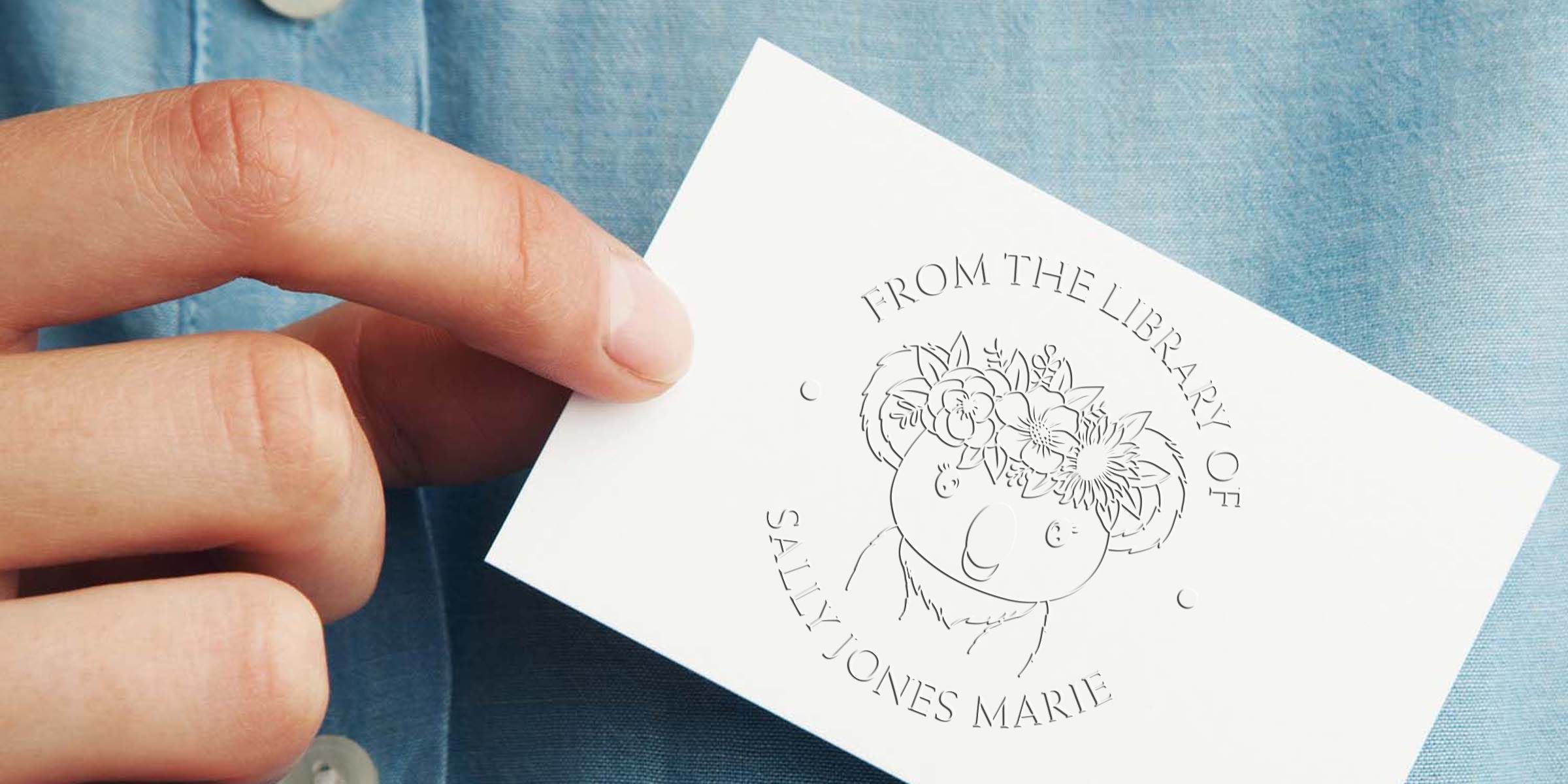 Hand holding a custom library bookplate card with floral bear illustration and “From the Library of Sally Jones Marie” text on a blue shirt background