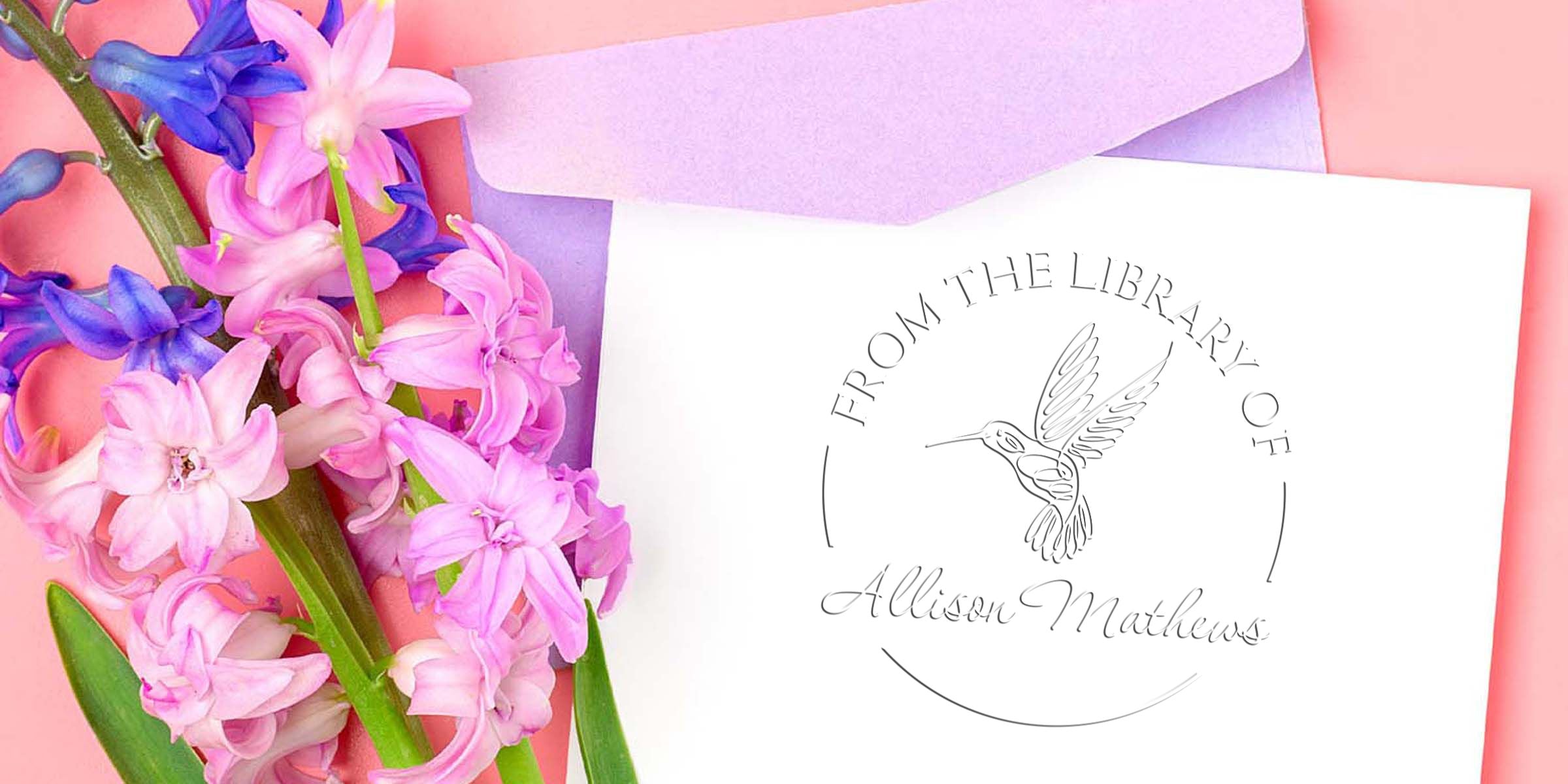 Pink and purple hyacinth flowers beside a personalized “From the Library Of Allison Mathews” bookplate card with hummingbird logo on a pastel pink background