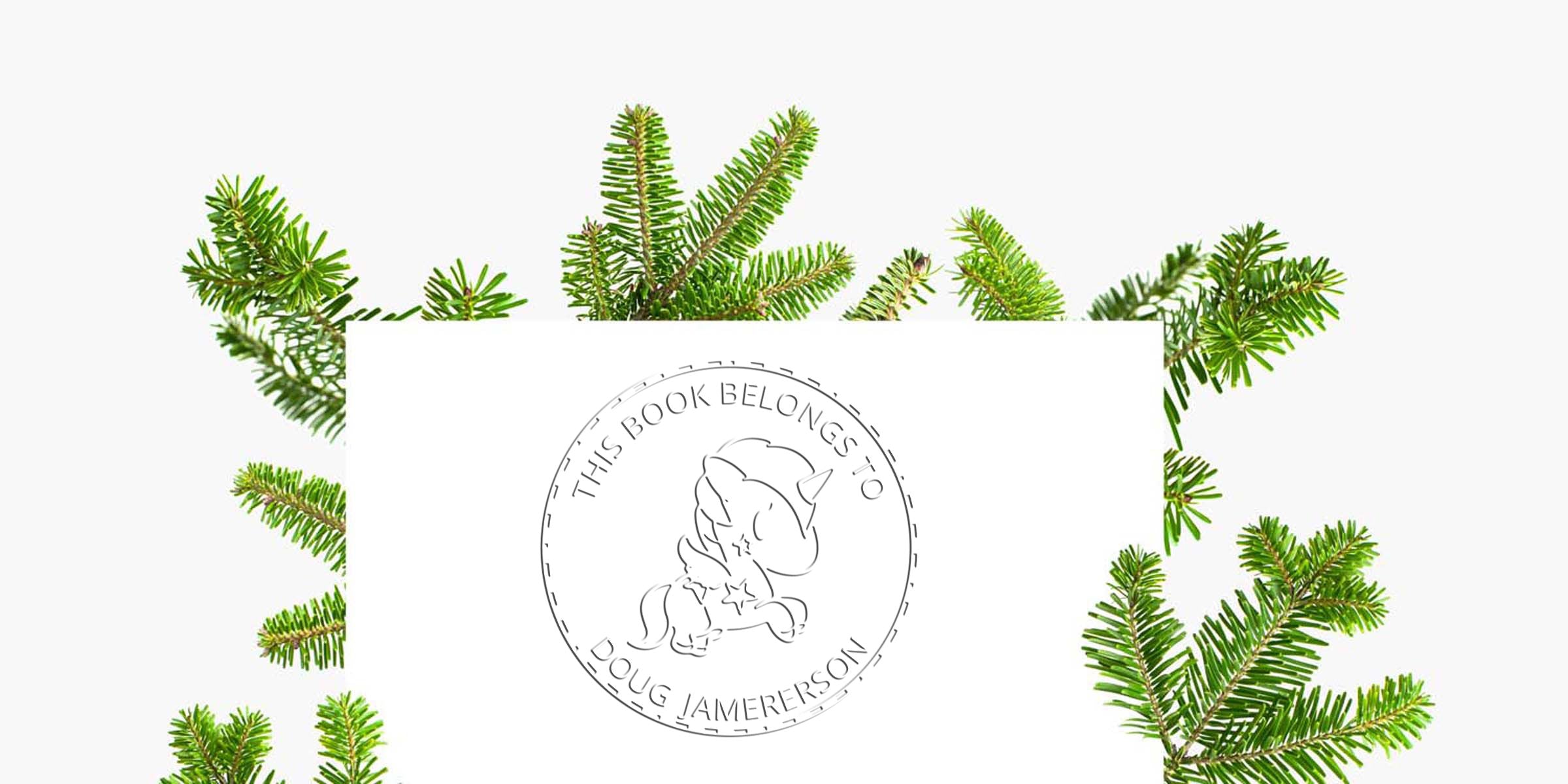 Personalized bookplate with unicorn stamp reading “This Book Belongs to Doug Jamerson,” surrounded by evergreen pine branches on a white background.