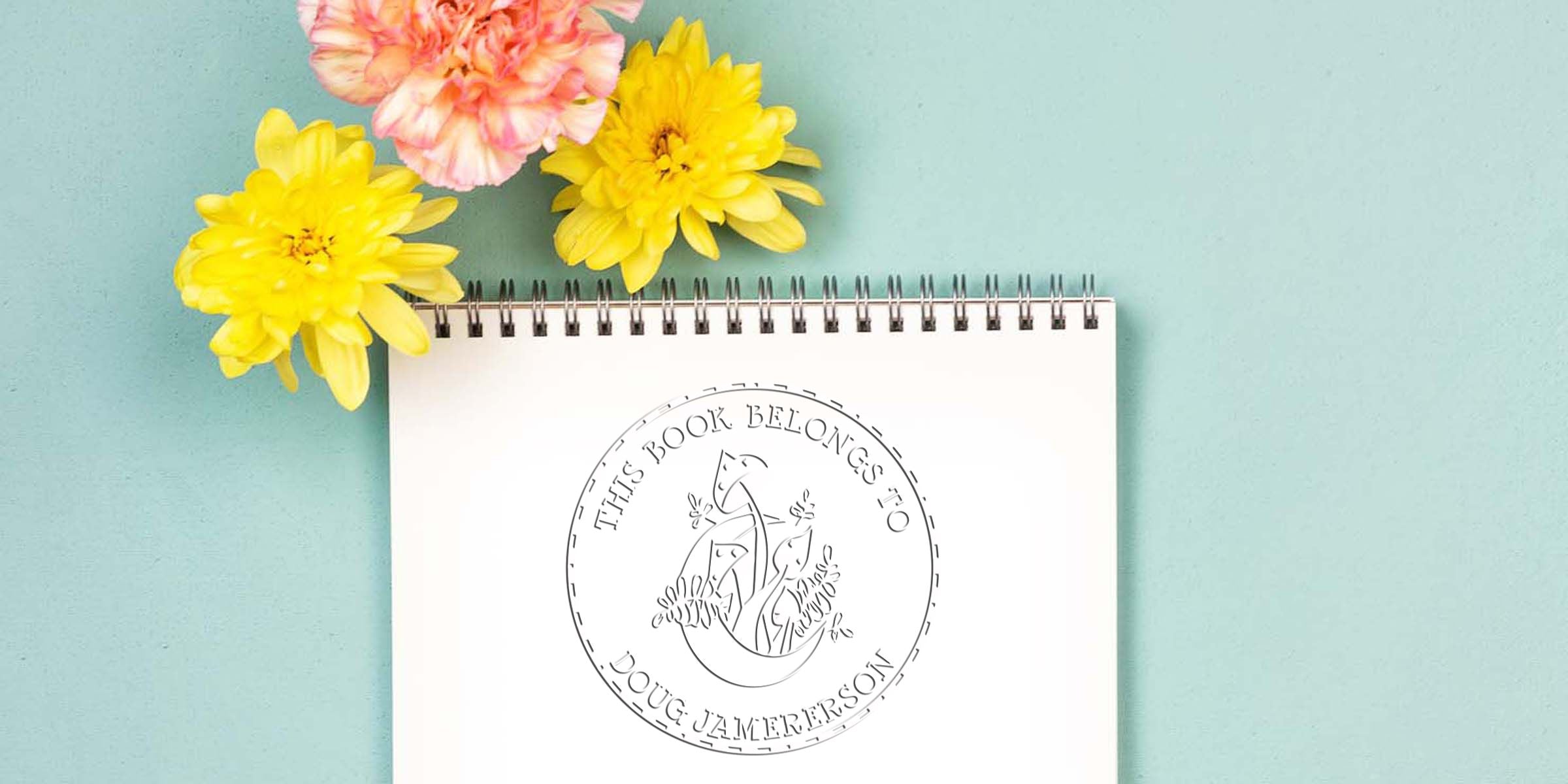 Spiral notebook with “This Book Belongs to Doug Jamerson” logo, surrounded by yellow and pink flowers on a pastel blue background