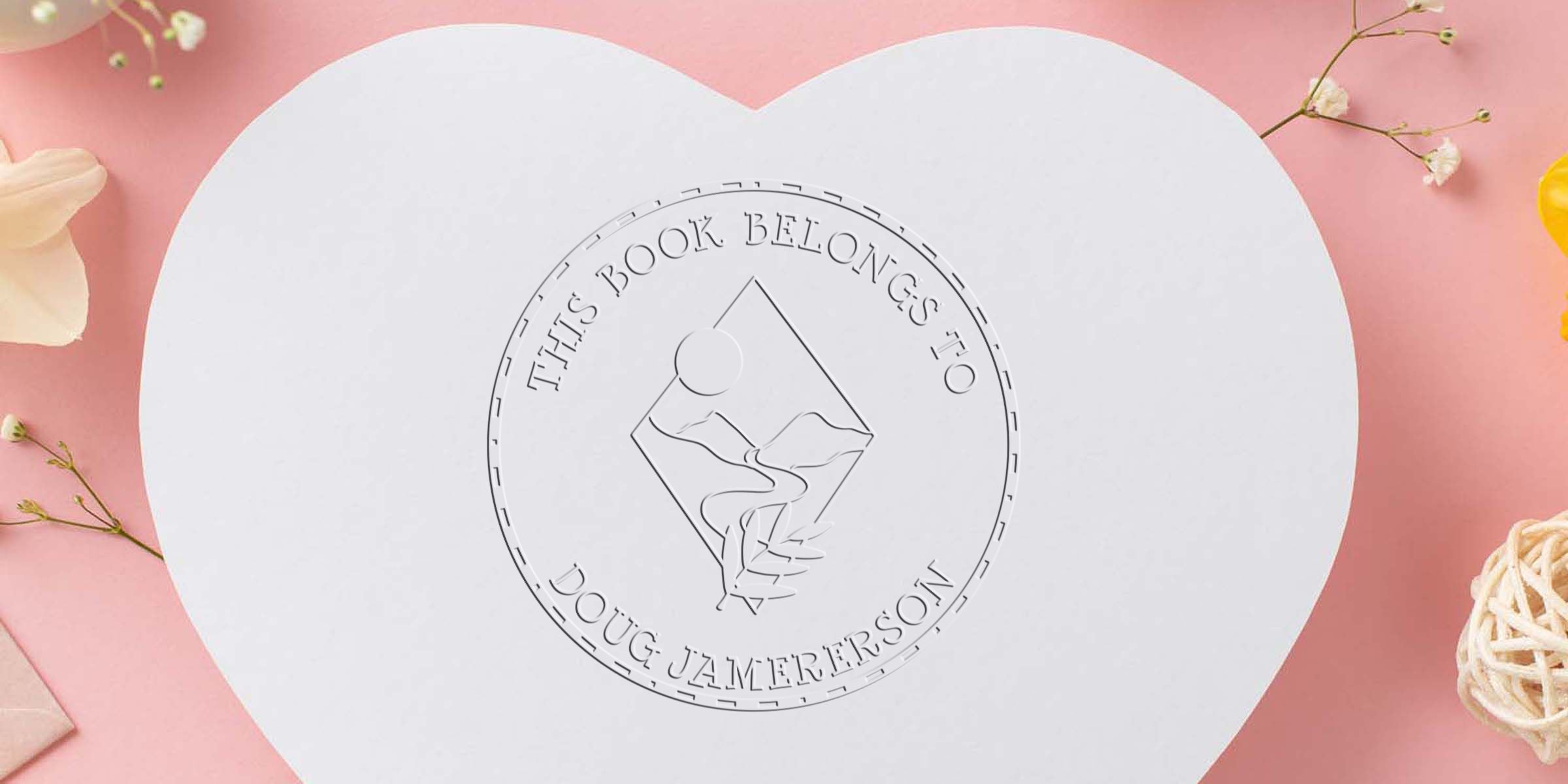Heart-shaped white personalized book cover with embossed logo reading This Book Belongs to Doug Jamerson on a pink floral background.