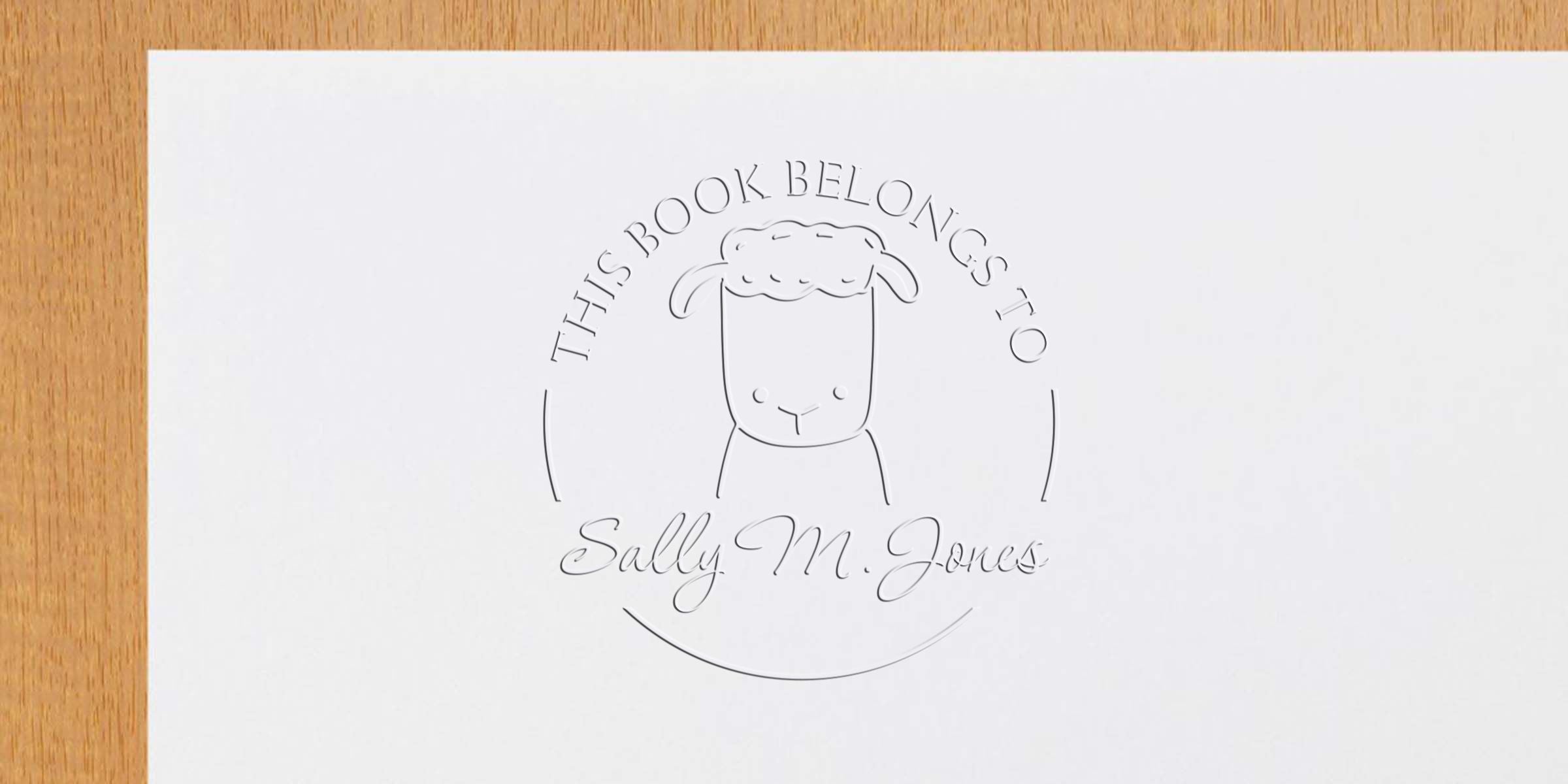 Embossed “This Book Belongs to Sally M. Jones” bookplate with a sheep illustration on white paper placed on a wooden surface