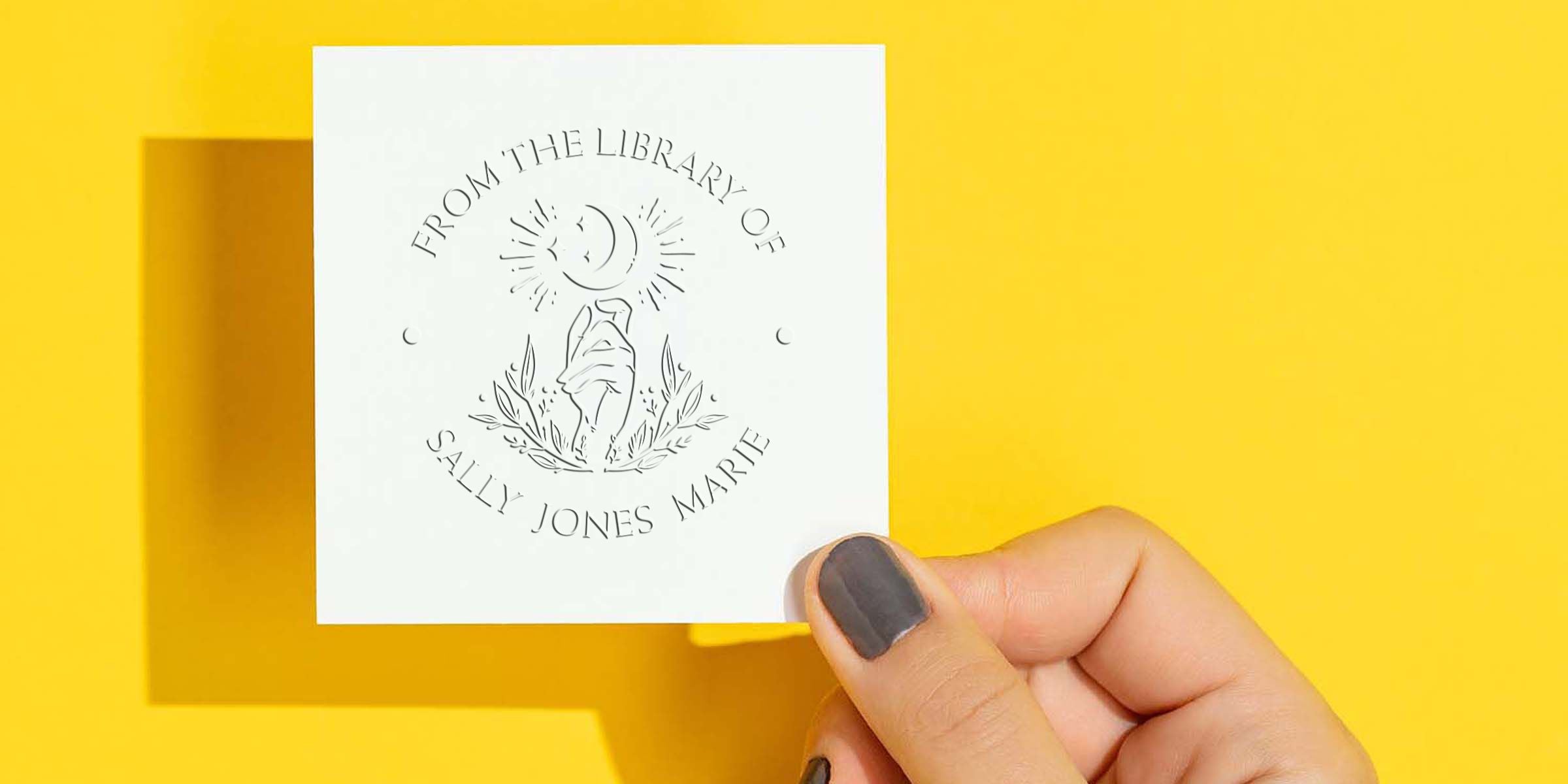 Hand holding a personalized “From the Library of Sally Jones Marie” bookplate card on a bright yellow background.