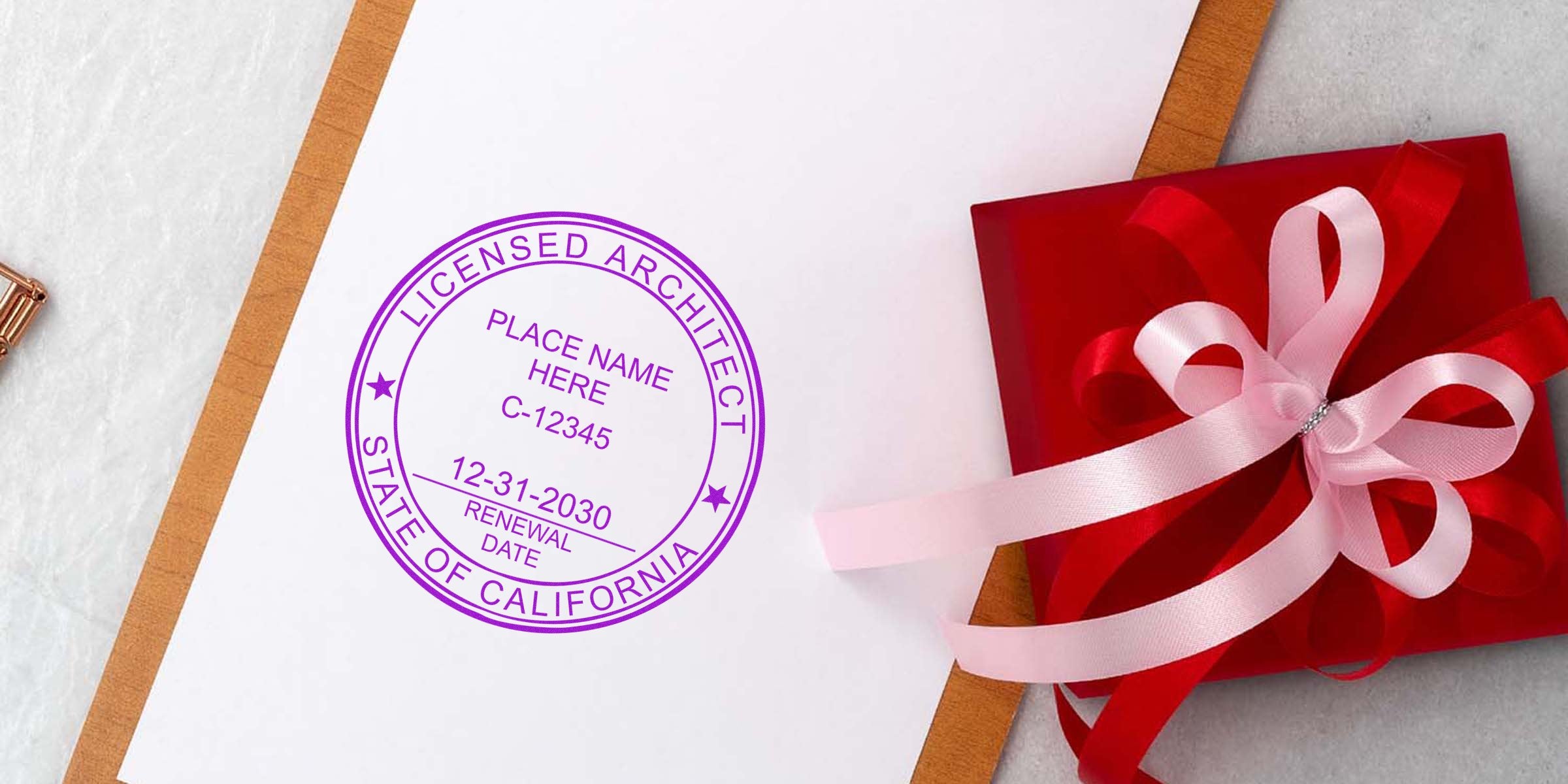California architect stamp on white paper next to a red gift box with pink ribbon on marble, symbolizing creative architectural design.