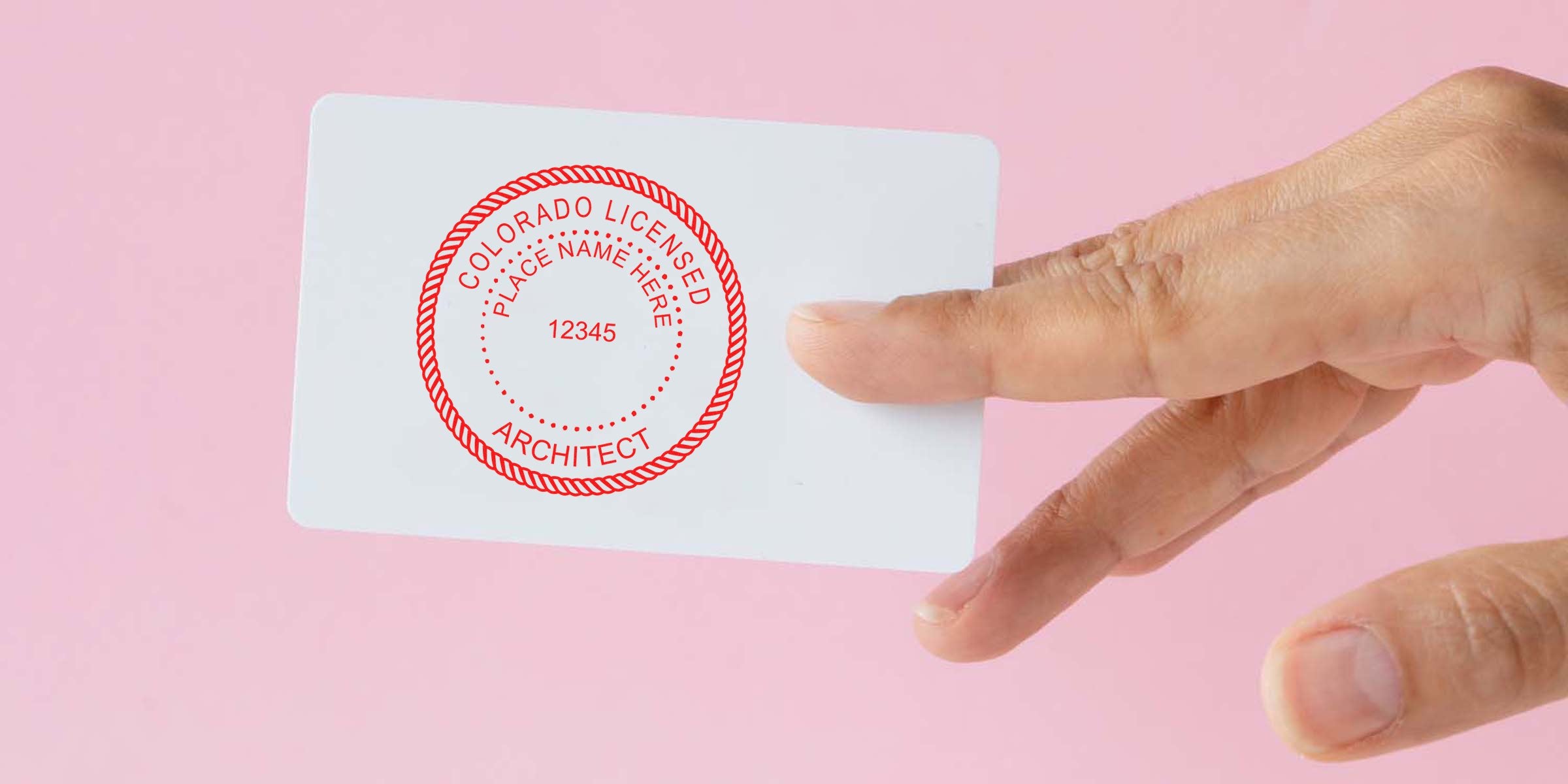Hand holding Colorado architect seal stamp card on pink background for license verification, showing Colorado architect seal and embosser guide.