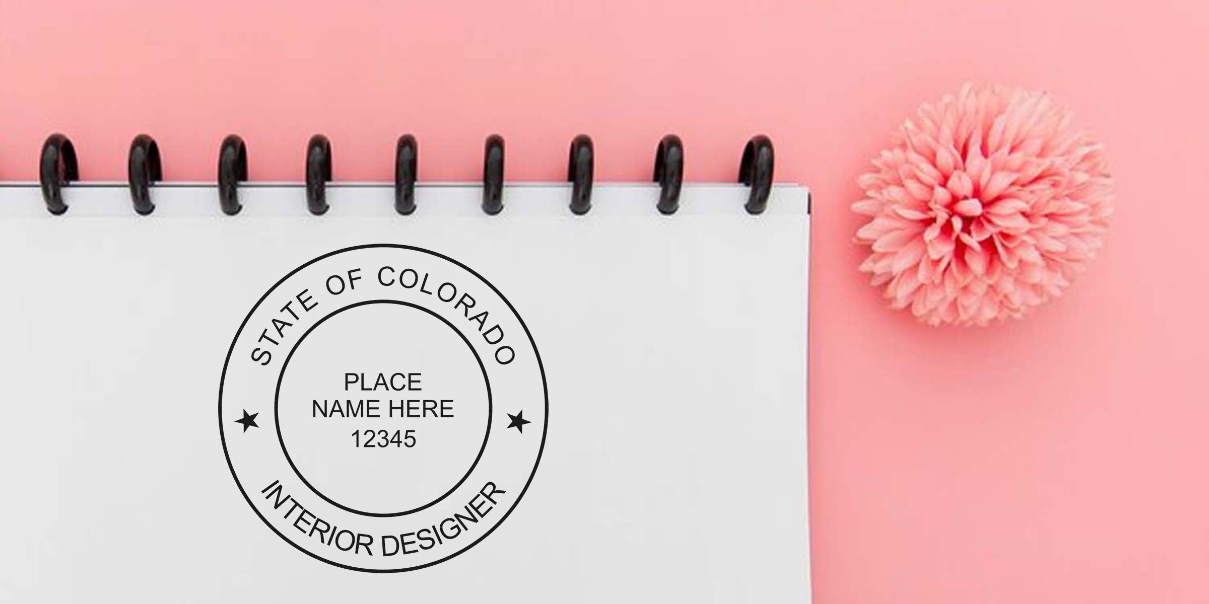 Colorado interior designer stamp with seal on white notebook, next to a pink flower on a pink background.