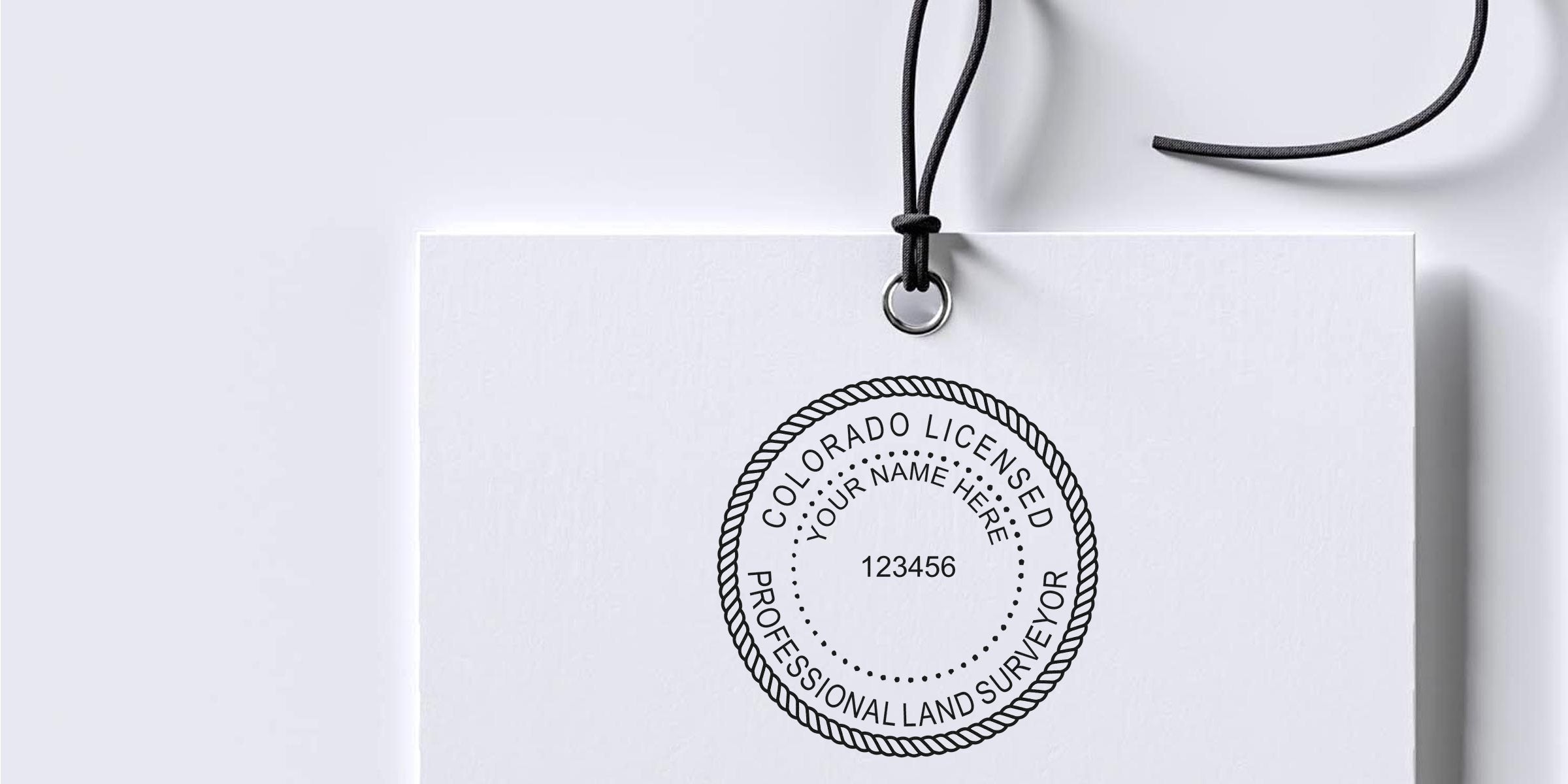 Colorado land surveyor stamp on white tag with black string, meeting land surveyor seal rules.