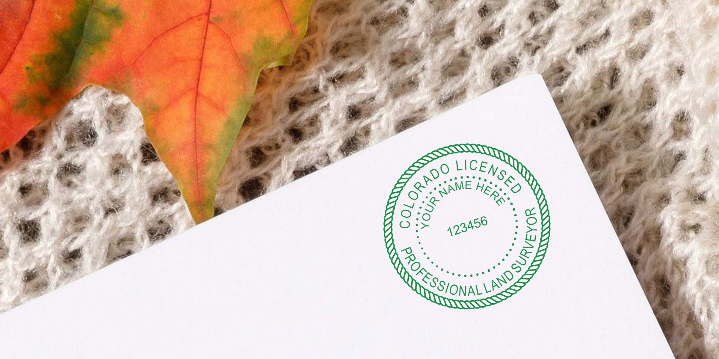 Colorado land surveyor stamp on white paper with autumn leaf and knitted fabric background, depicting a Colorado land surveyor stamp order.