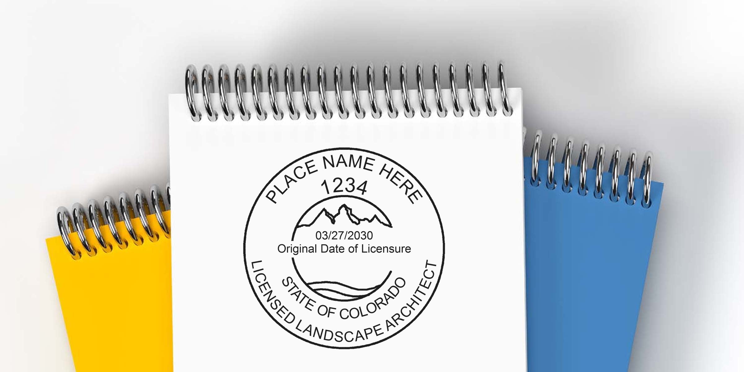 Colorado licensed landscape architect stamp on white notepad, with yellow and blue notepads behind, highlighting the license and regulations for Colorado landscape architects.