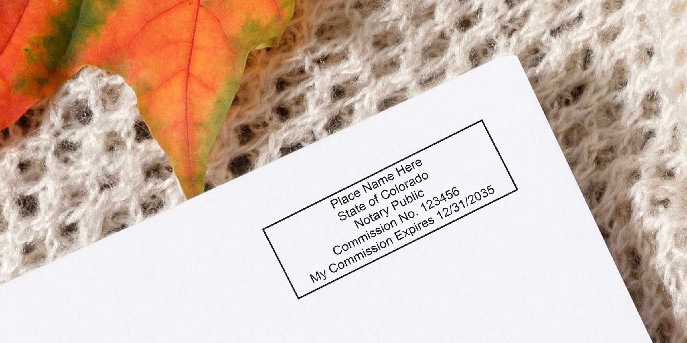 Colorado notary public commission certificate on white paper with autumn leaf and knitted fabric background, showing Colorado notary stamp per notary stamp law.