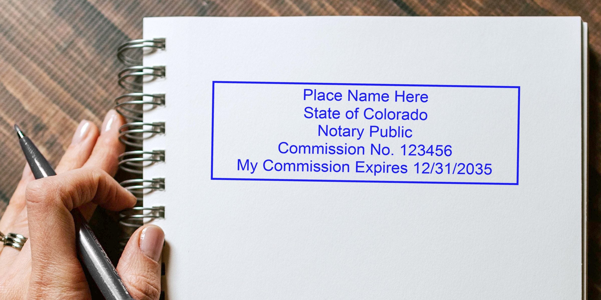 Colorado notary public stamp on white spiral notebook with hand holding pen, related to Colorado notary stamp renewal and renewal requirements.