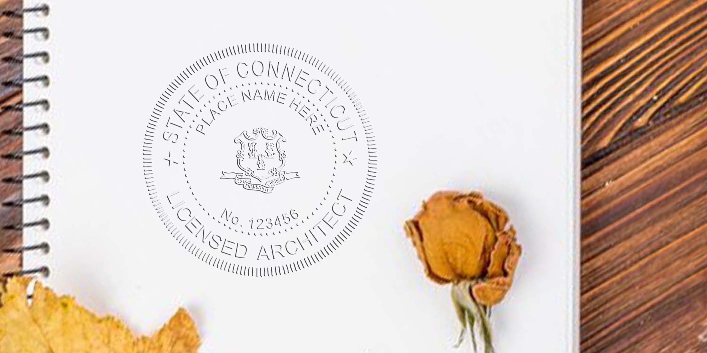 Connecticut architect stamp on notebook with dried flower and leaf on wooden table, showing licensed architect seal and promoting online architect stamp purchase.