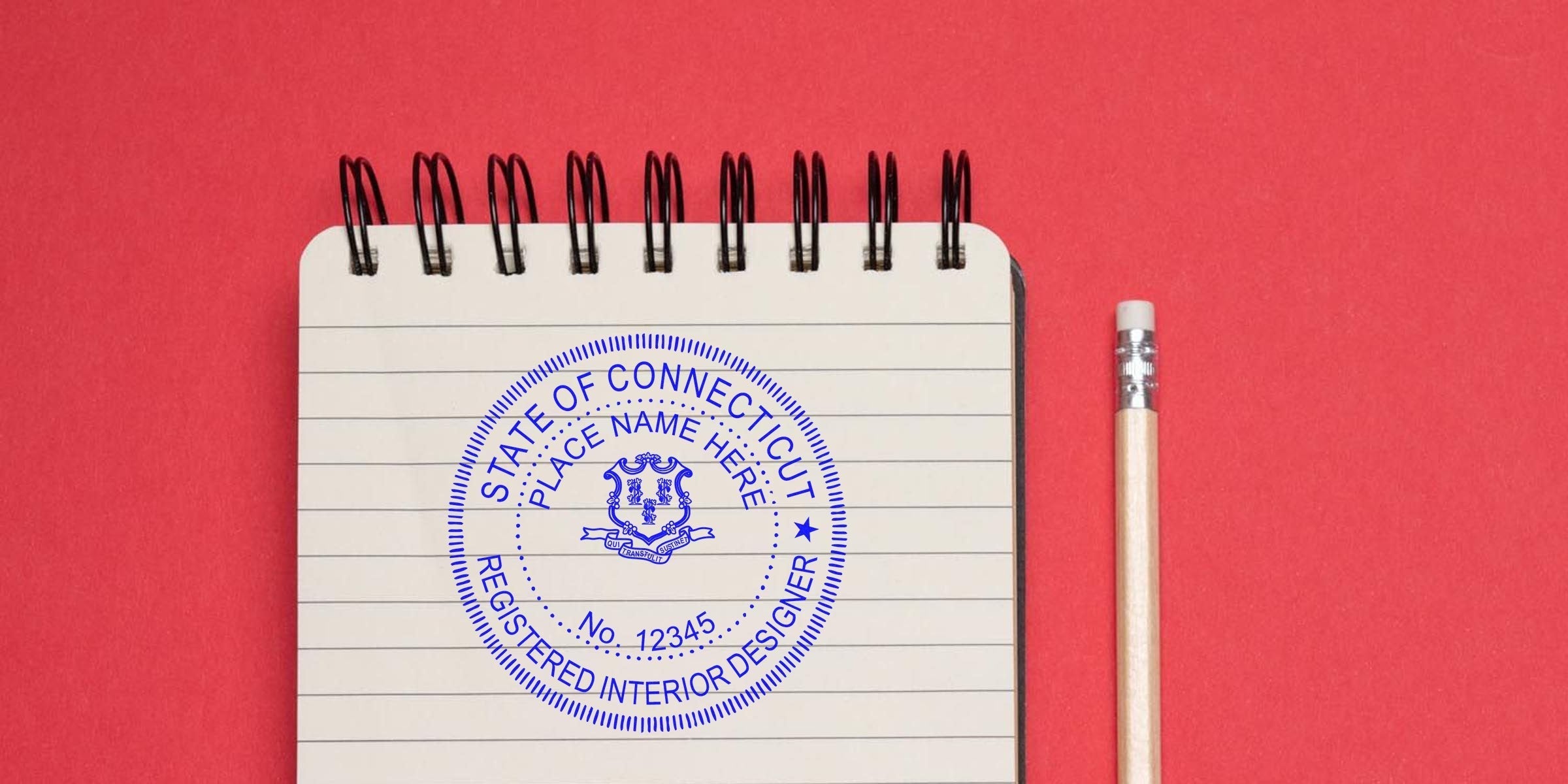 Connecticut interior designer stamps with the registered seal on a notebook and pencil, symbolizing interior design certification, set against a red background.