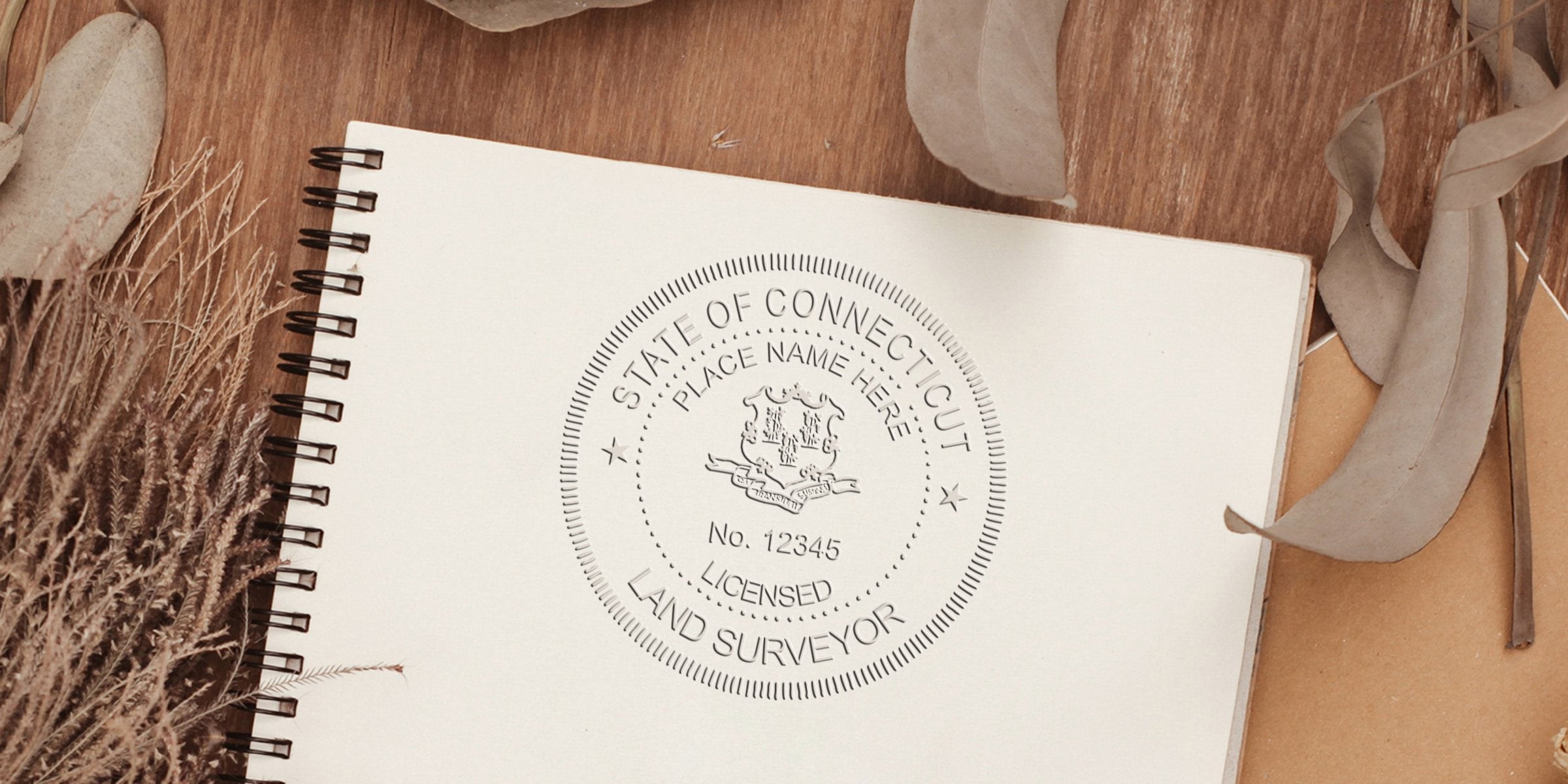 Connecticut land surveyor seal on notebook with dried leaves, wooden background, and official notary stamp meeting land surveyor seal requirements.