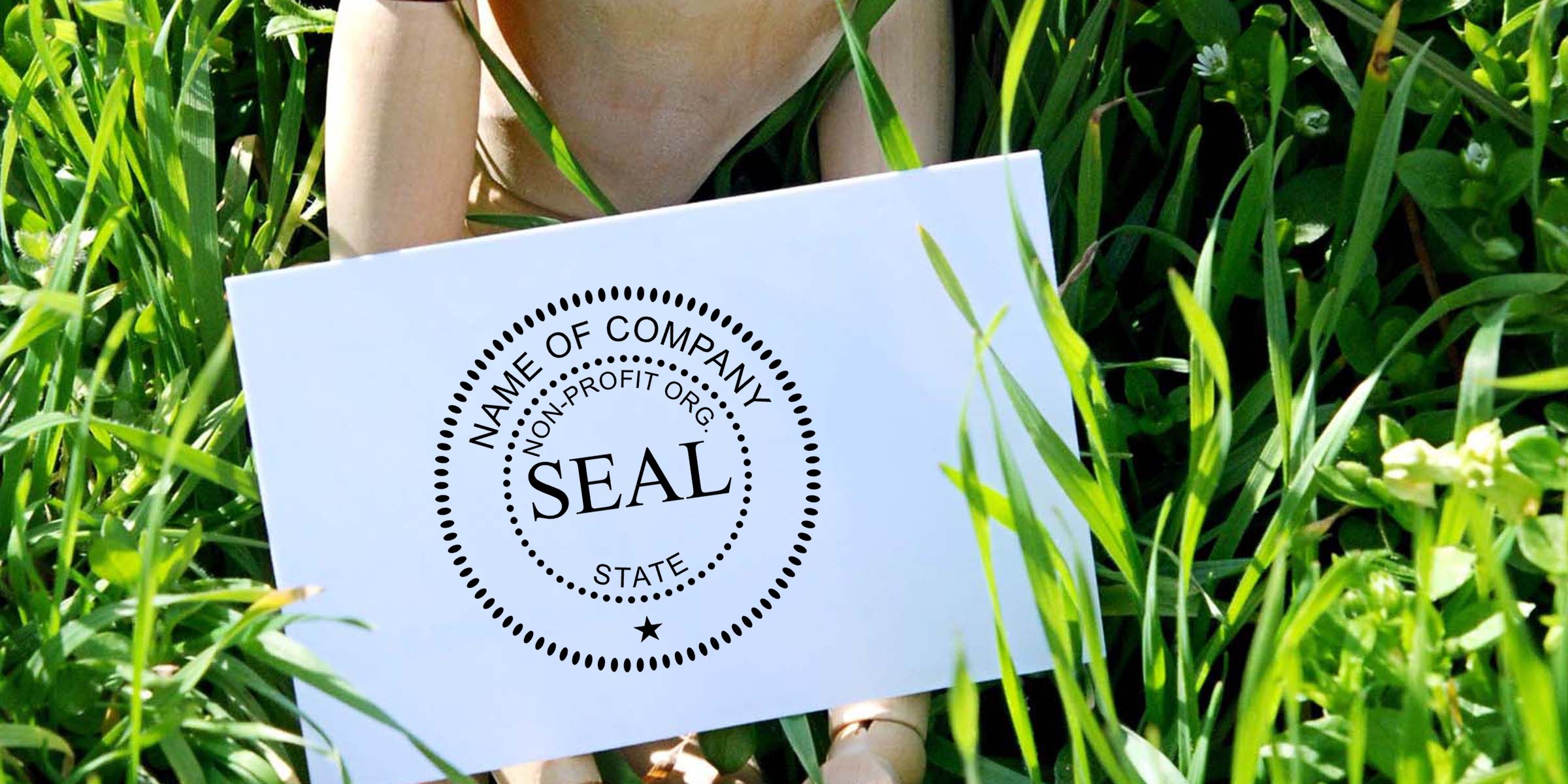 Mannequin torso holding a white nonprofit company seal sign in green grass outdoors