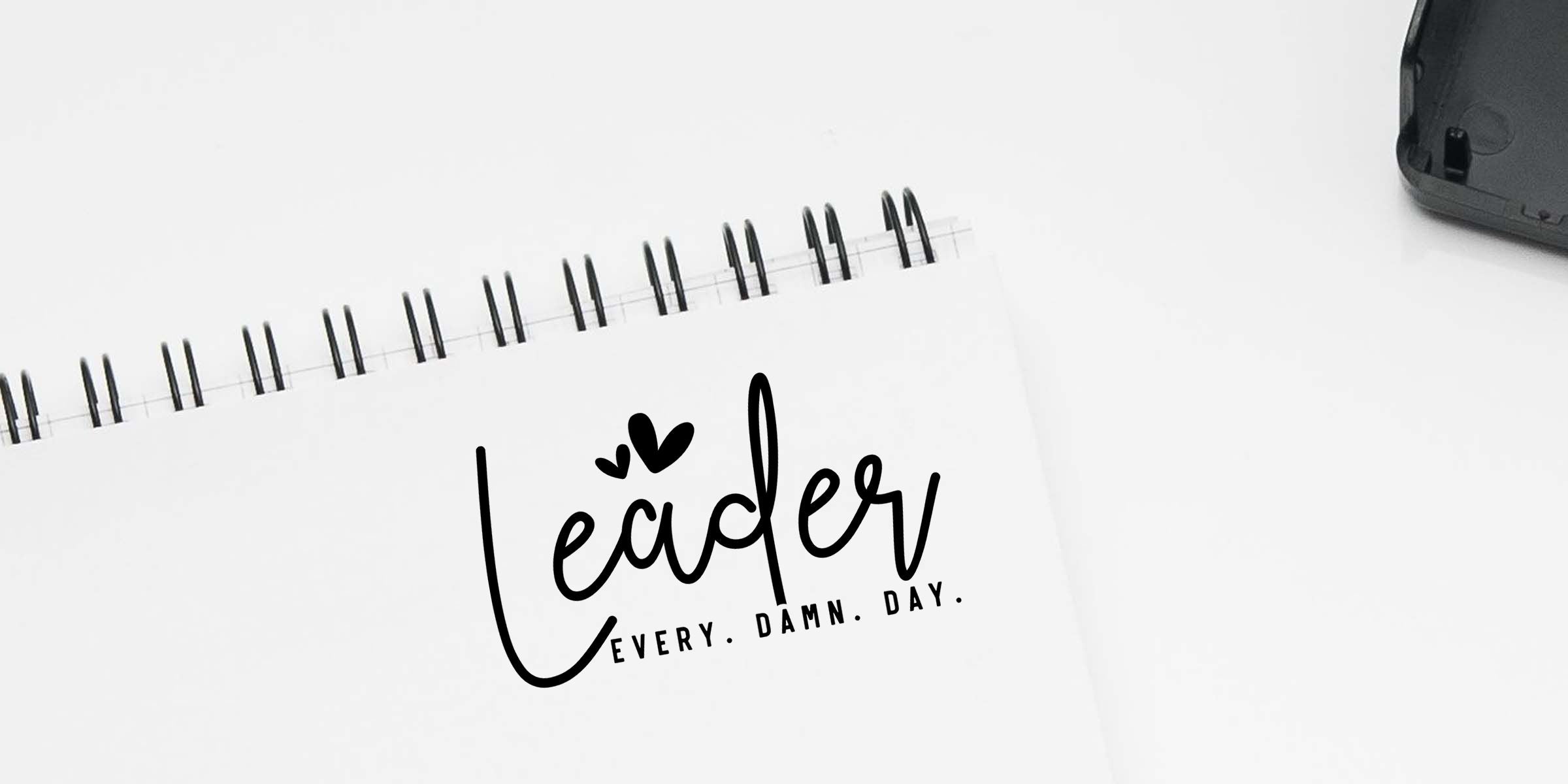 Minimalist spiral notebook with “Leader” motivational quote and “Every. Damn. Day.” text on a white desk background