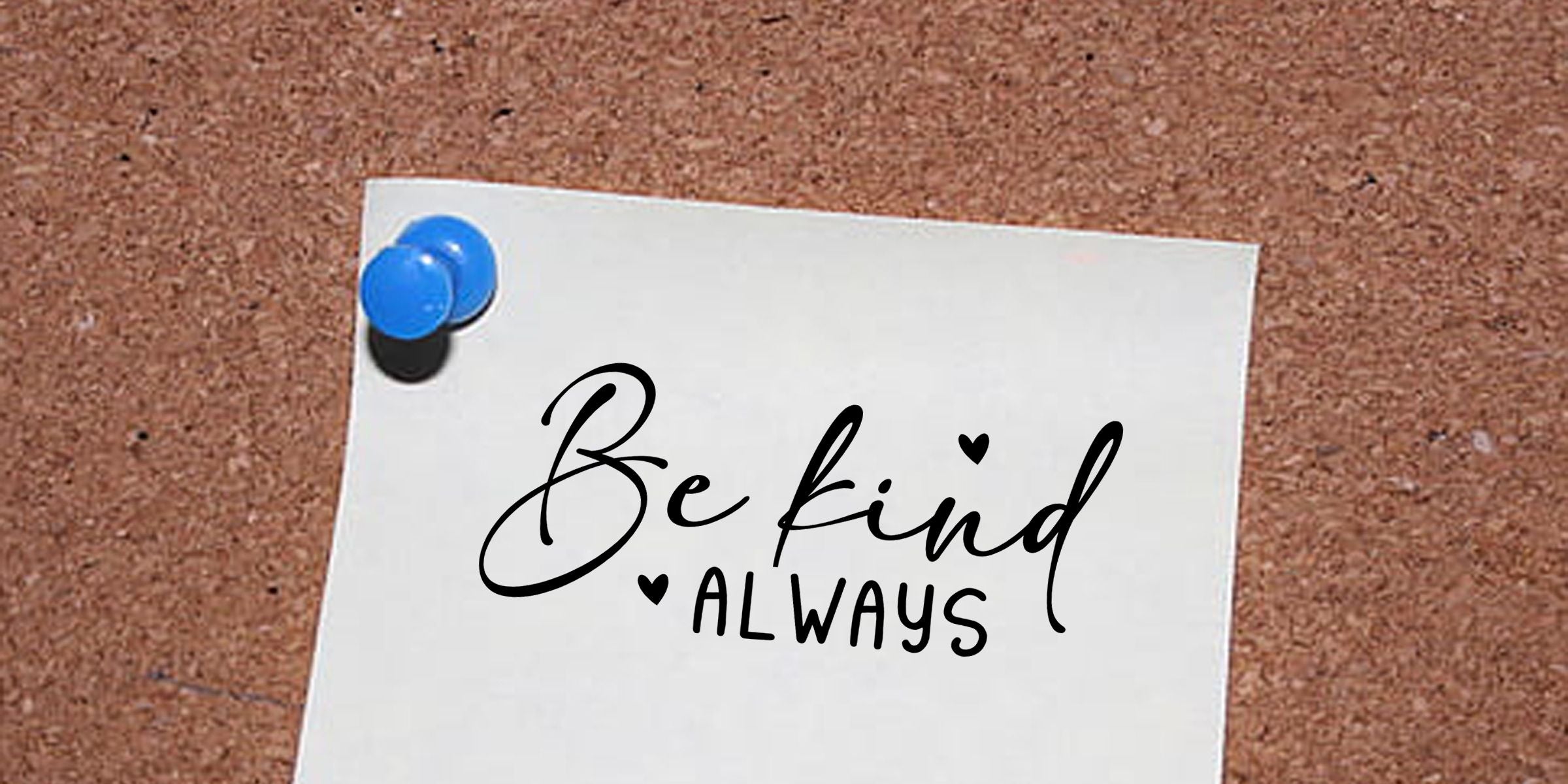 White note pinned to a corkboard with a blue pushpin, displaying the motivational message “Be kind always” with small heart symbols.