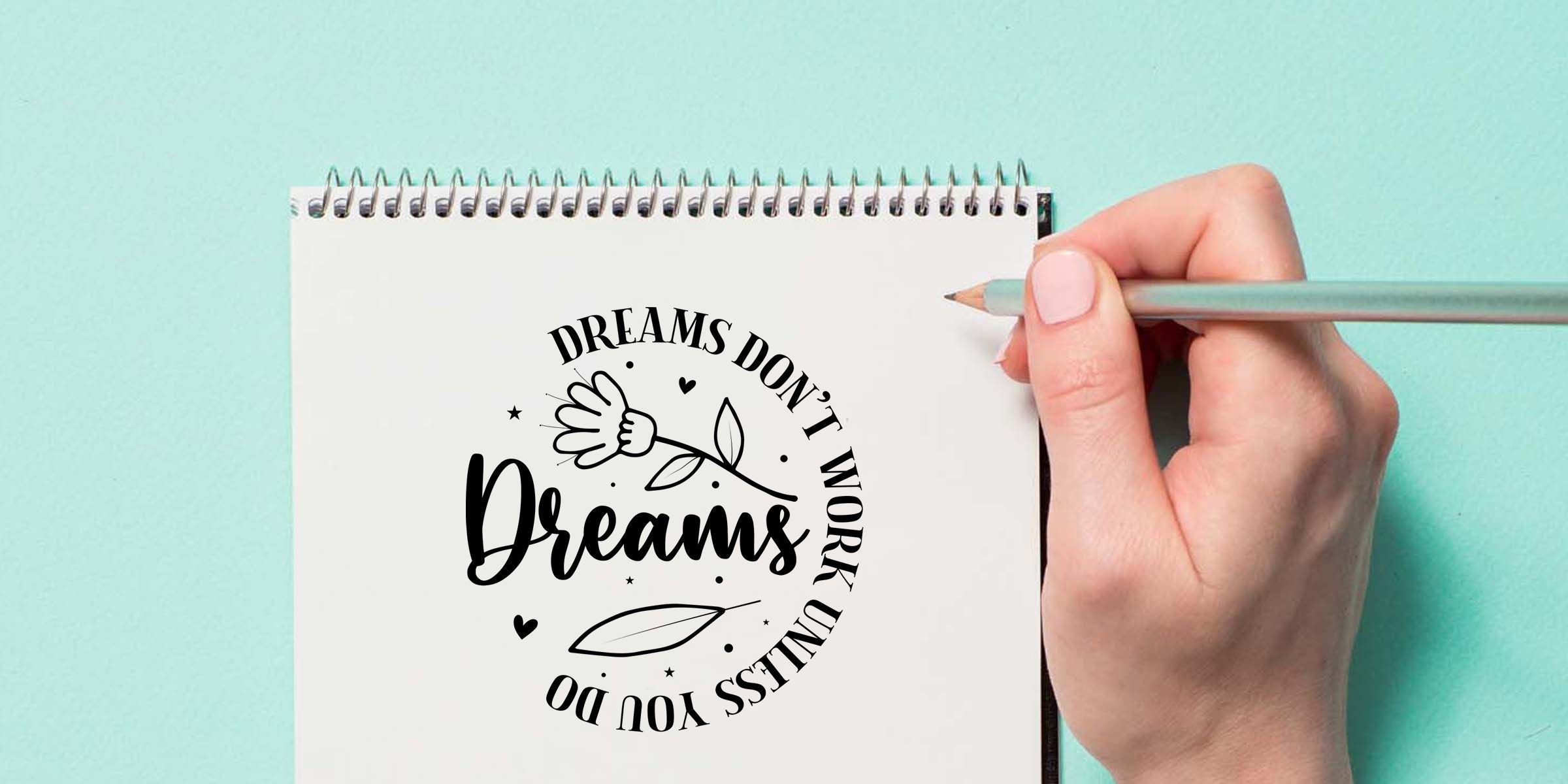 Hand holding a pencil over a spiral notebook showing the motivational quote “Dreams don’t work unless you do” with floral artwork on a mint green background.