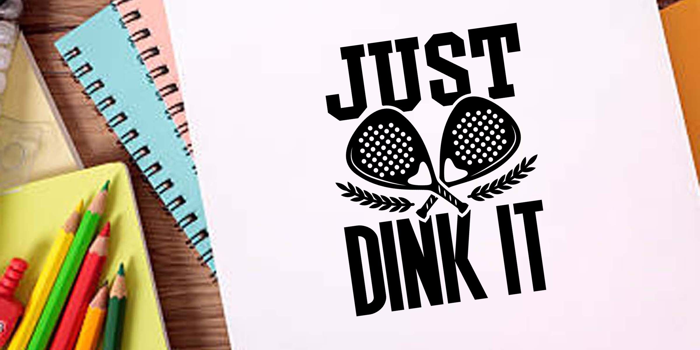 Notebook with “Just Dink It” pickleball design, crossed paddles graphic, and colorful school supplies on a desk