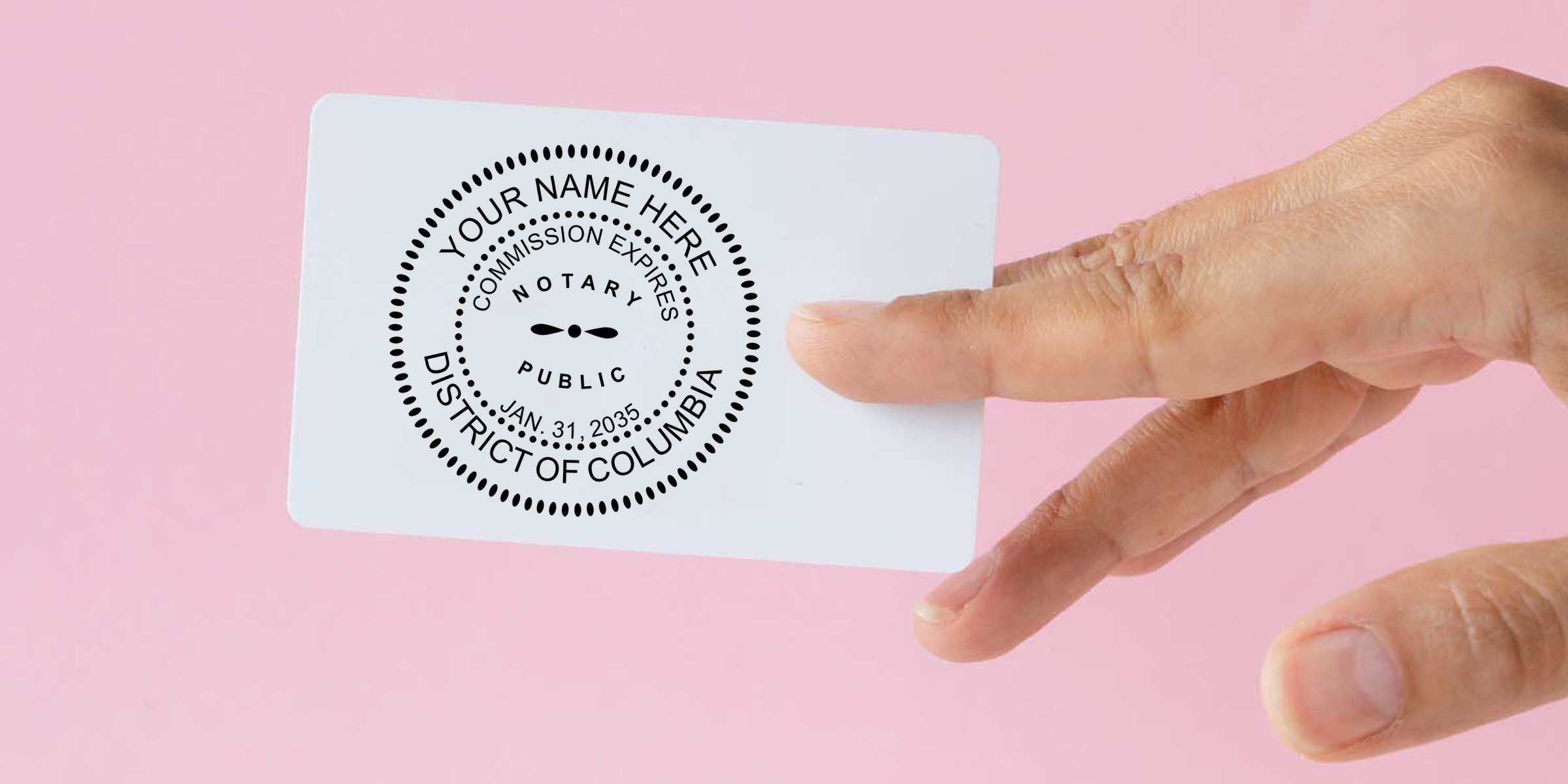 Hand holding a white notary public seal card with District of Columbia commission stamp on a pink background