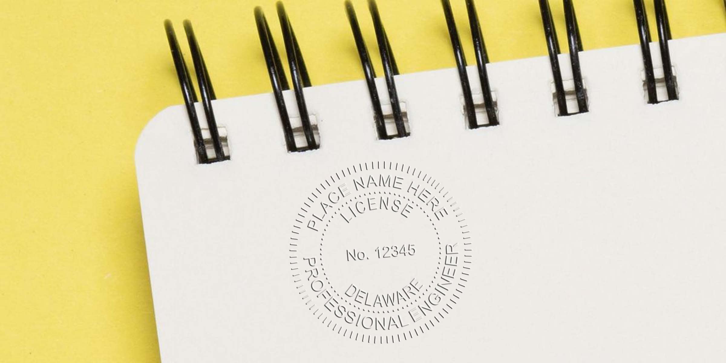 Delaware PE stamp on white spiral notebook set against a yellow background, showcasing a custom engineering stamp design.