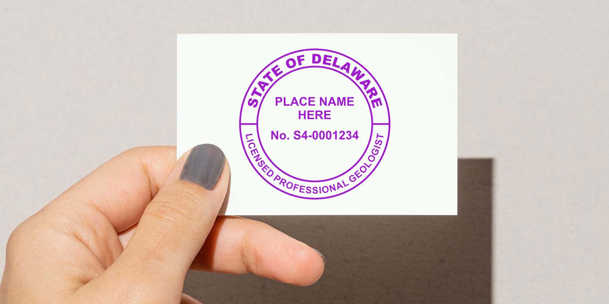 Hand holding a Delaware Professional Geologist Seal stamp with purple ink on white paper, used to obtain a Geologist Seal in Delaware.