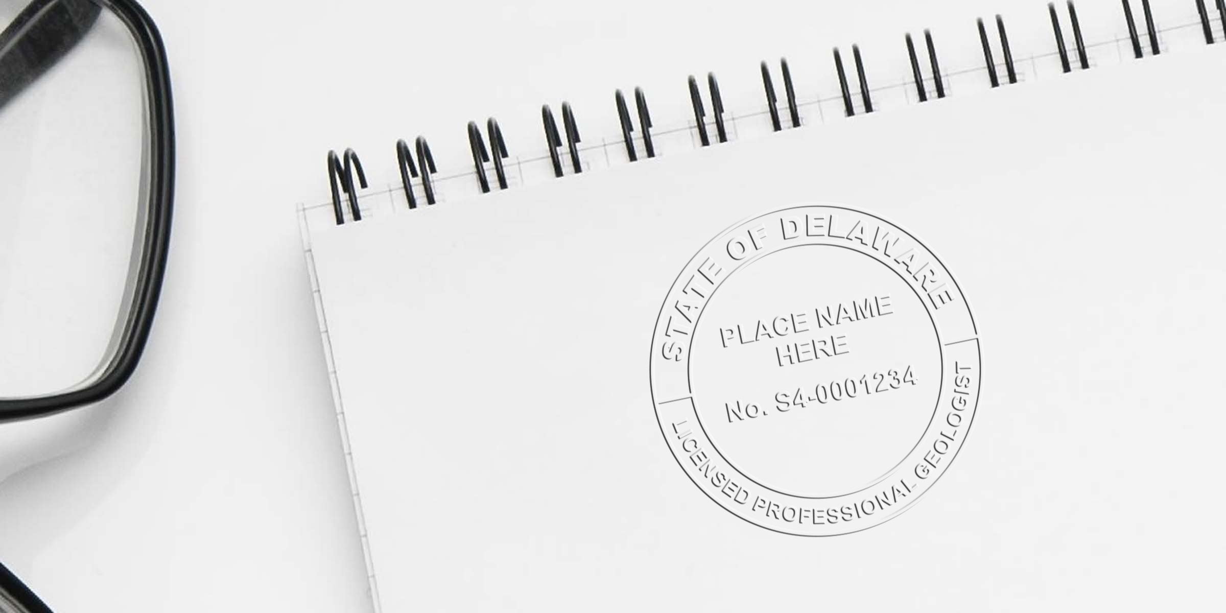 Delaware Geologist License embossed seal on white spiral notebook with black glasses nearby, showing Geologist Stamp Delaware.