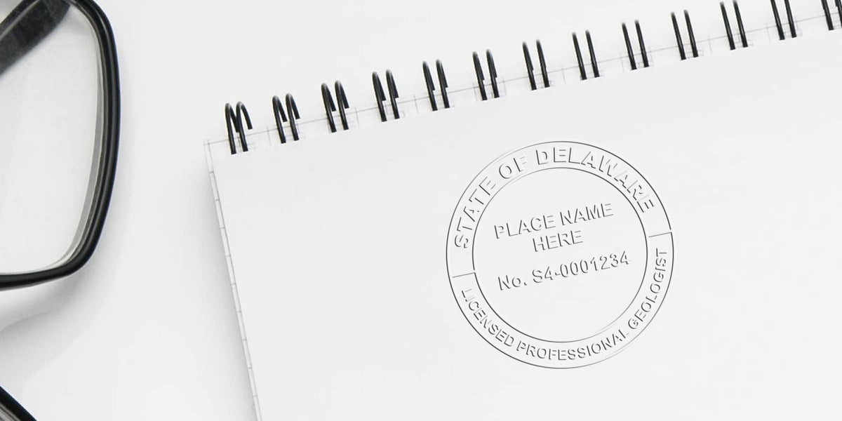 Delaware Geologist License embossed seal on white spiral notebook with black glasses nearby, showing Geologist Stamp Delaware.