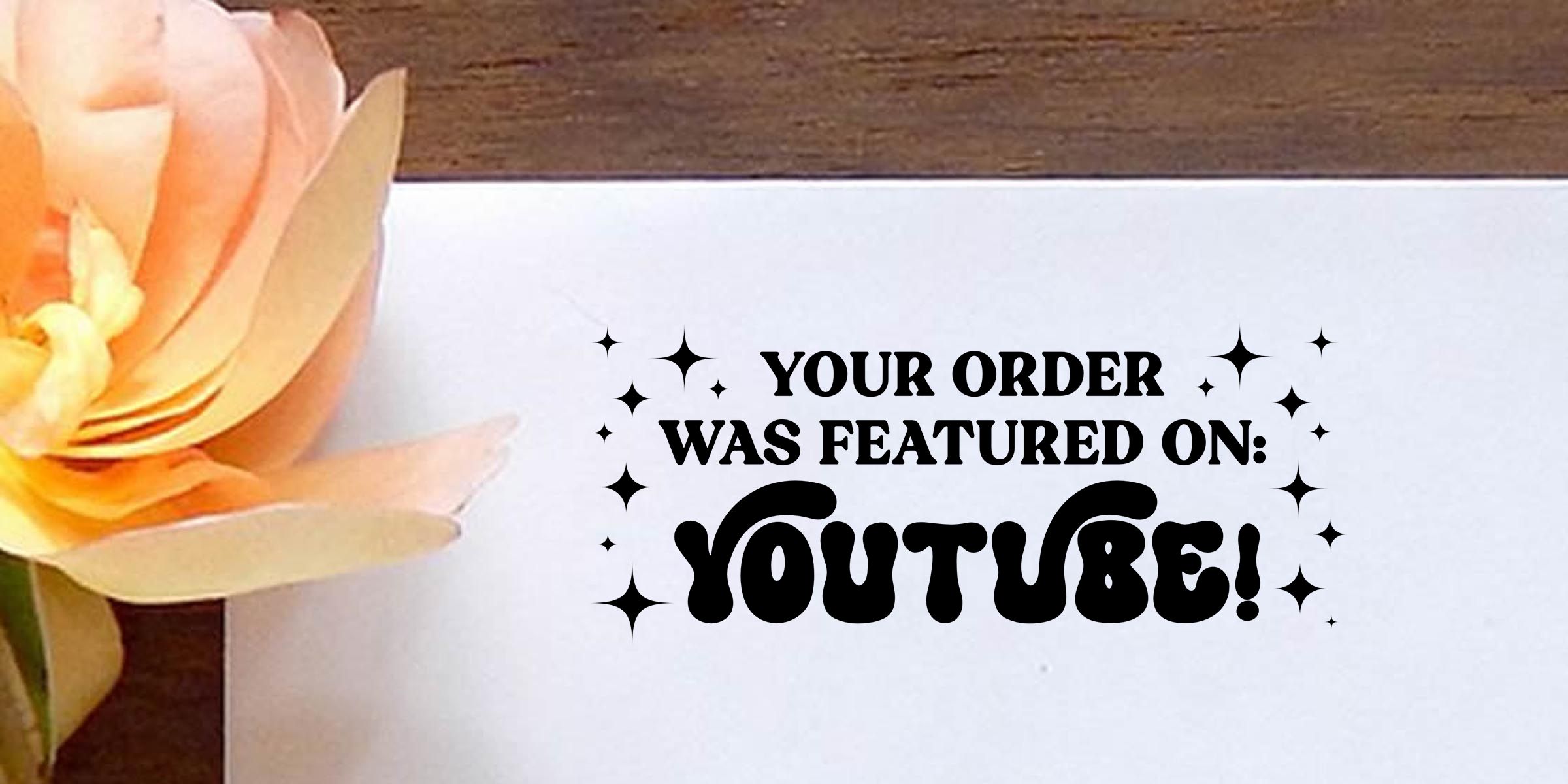 Decorative floral card with bold text reading “Your order was featured on: YouTube!” on a white background with sparkling accents and a pastel flower on the left.
