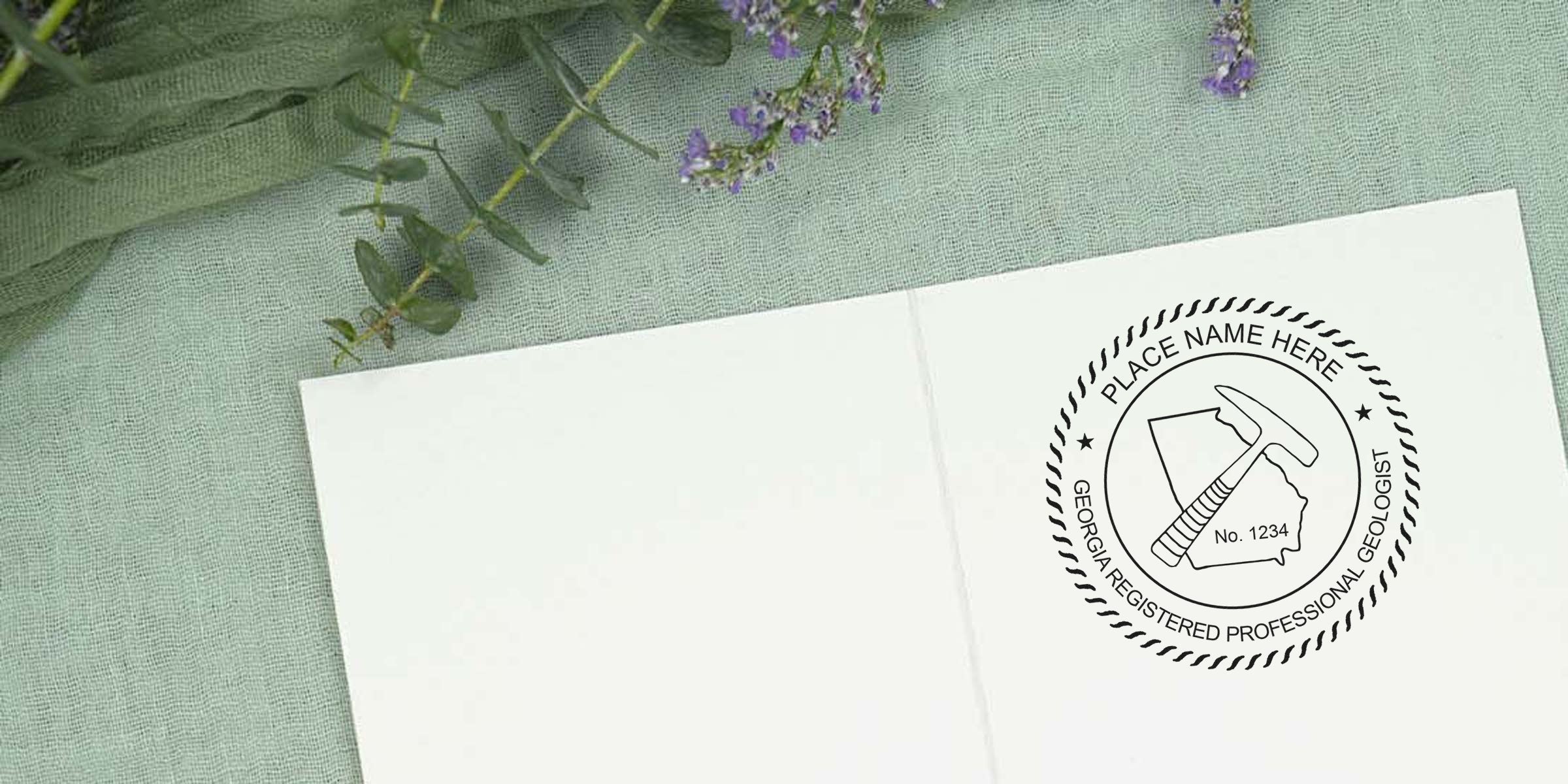 Georgia geologist license stamp with registered professional geologist seal, rock hammer, and state outline on white paper, placed on green fabric with purple flowers, showcasing Georgia geologist stamp requirements.