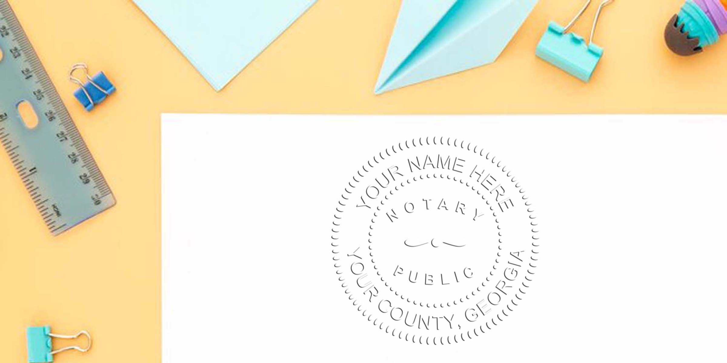 Custom Georgia notary seal stamp on white paper with office supplies on yellow background, personalized for Georgia county, featured in a notary stamp guide.