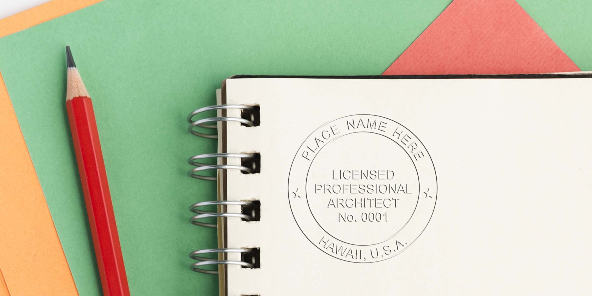 Red pencil on colorful paper beside a spiral notebook with a Hawaii architect stamp and embossed design.