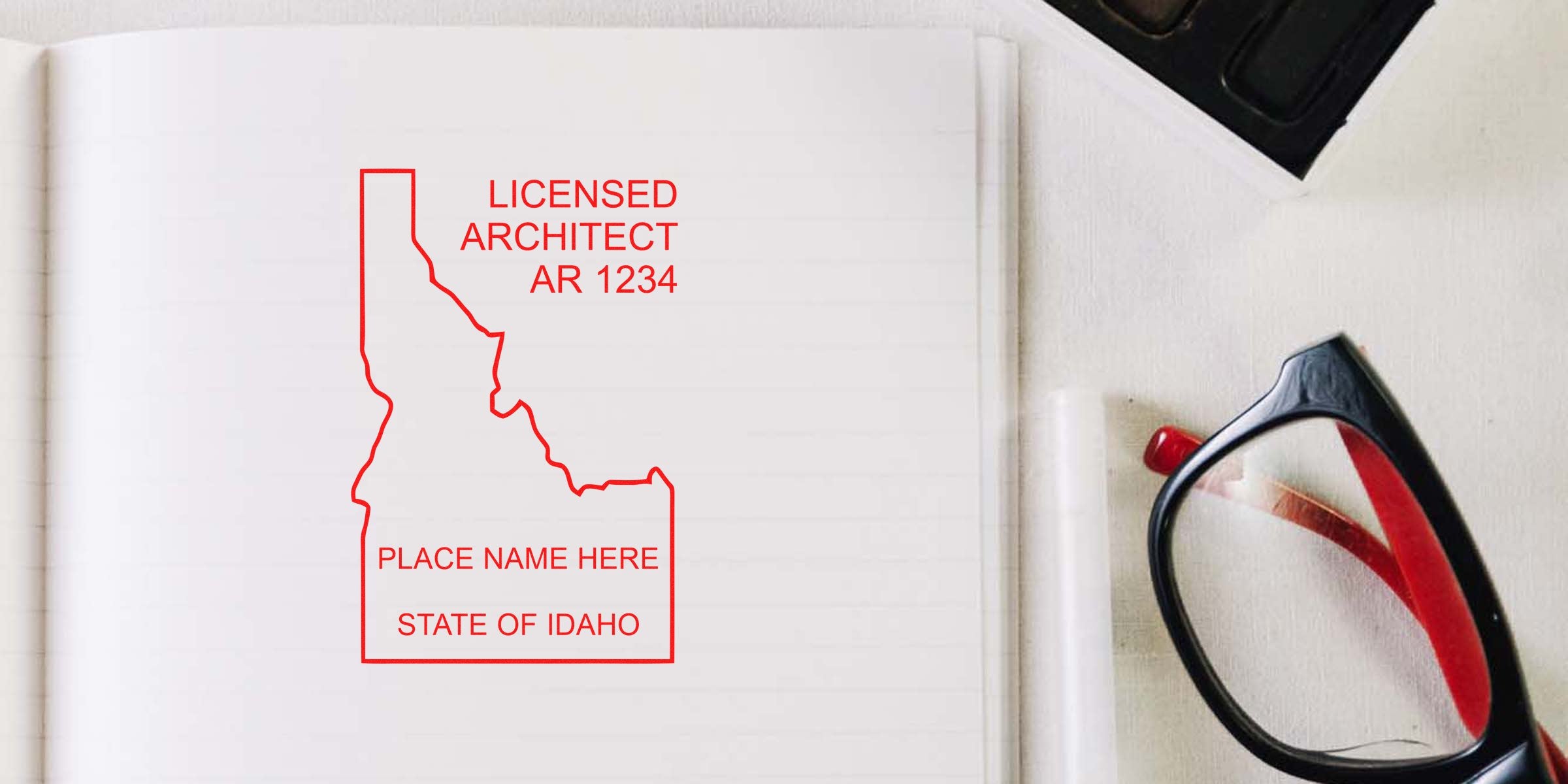 Idaho architect seal embossed on notebook beside black and red glasses on white desk, highlighting Idaho architect embosser requirements.