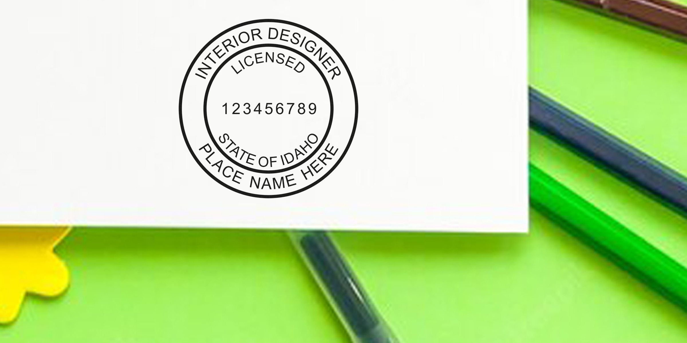 Licensed interior designer stamp for Idaho on white paper, surrounded by green and yellow office supplies, adhering to seal design guidelines.