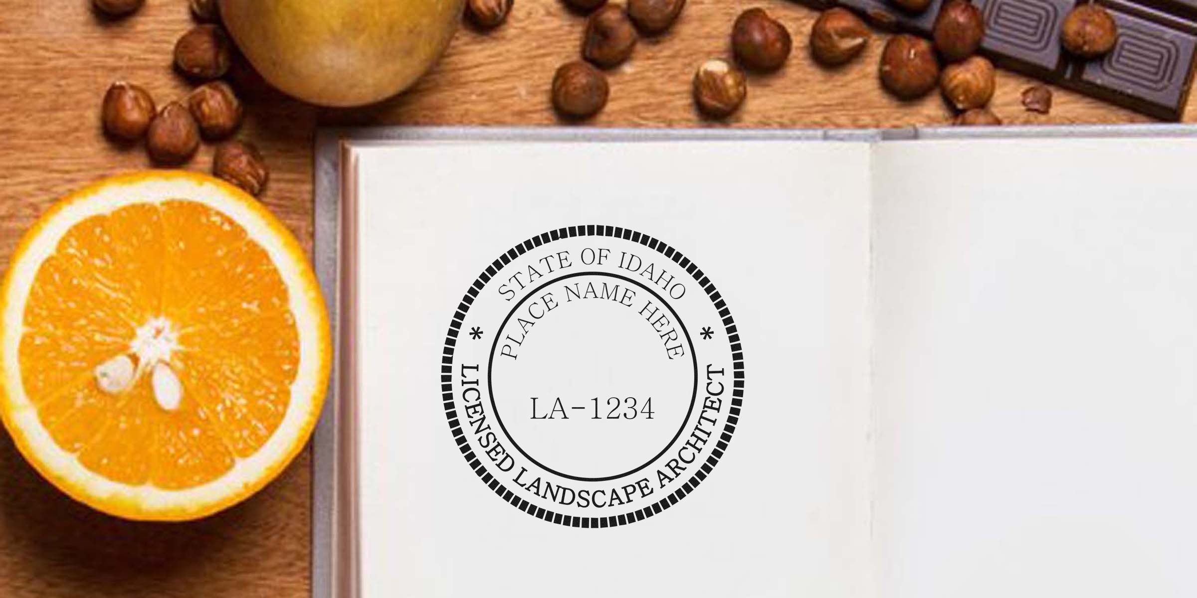 Idaho landscape architect seal embossed on notebook, with orange slice, hazelnuts, and chocolate on wooden table, showing seal embosser in use.