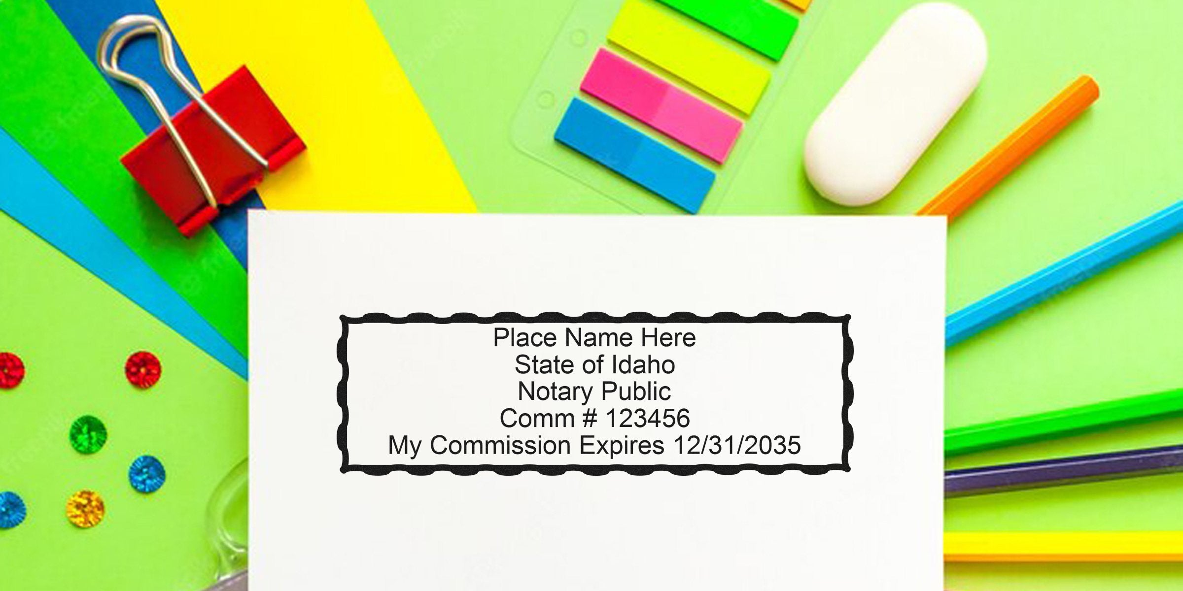 Idaho notary stamp with commission number and expiration date on white paper, surrounded by colorful office supplies, highlighting where to buy a notary stamp online.