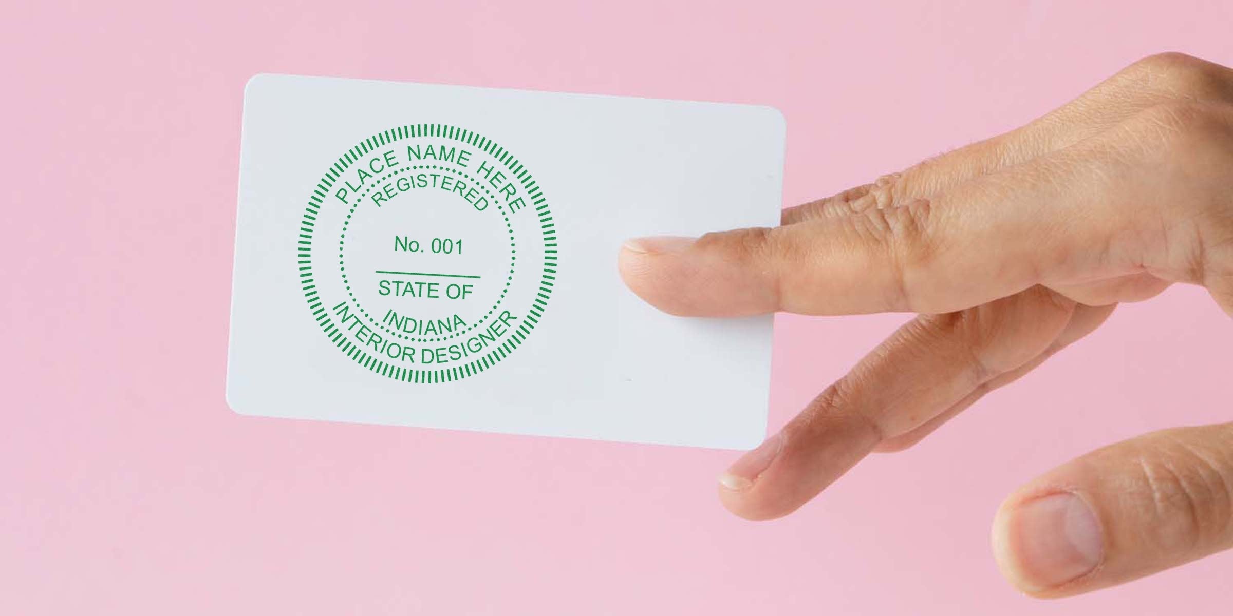 Hand holding an Indiana interior designer certification card with the Indiana seal and interior design stamp on a pink background.
