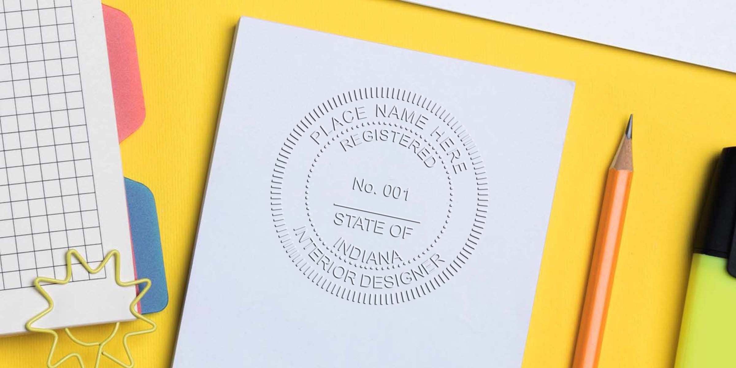 Indiana interior designer certification embossed on white paper with office supplies on a yellow background, showcasing an interior design stamp online.