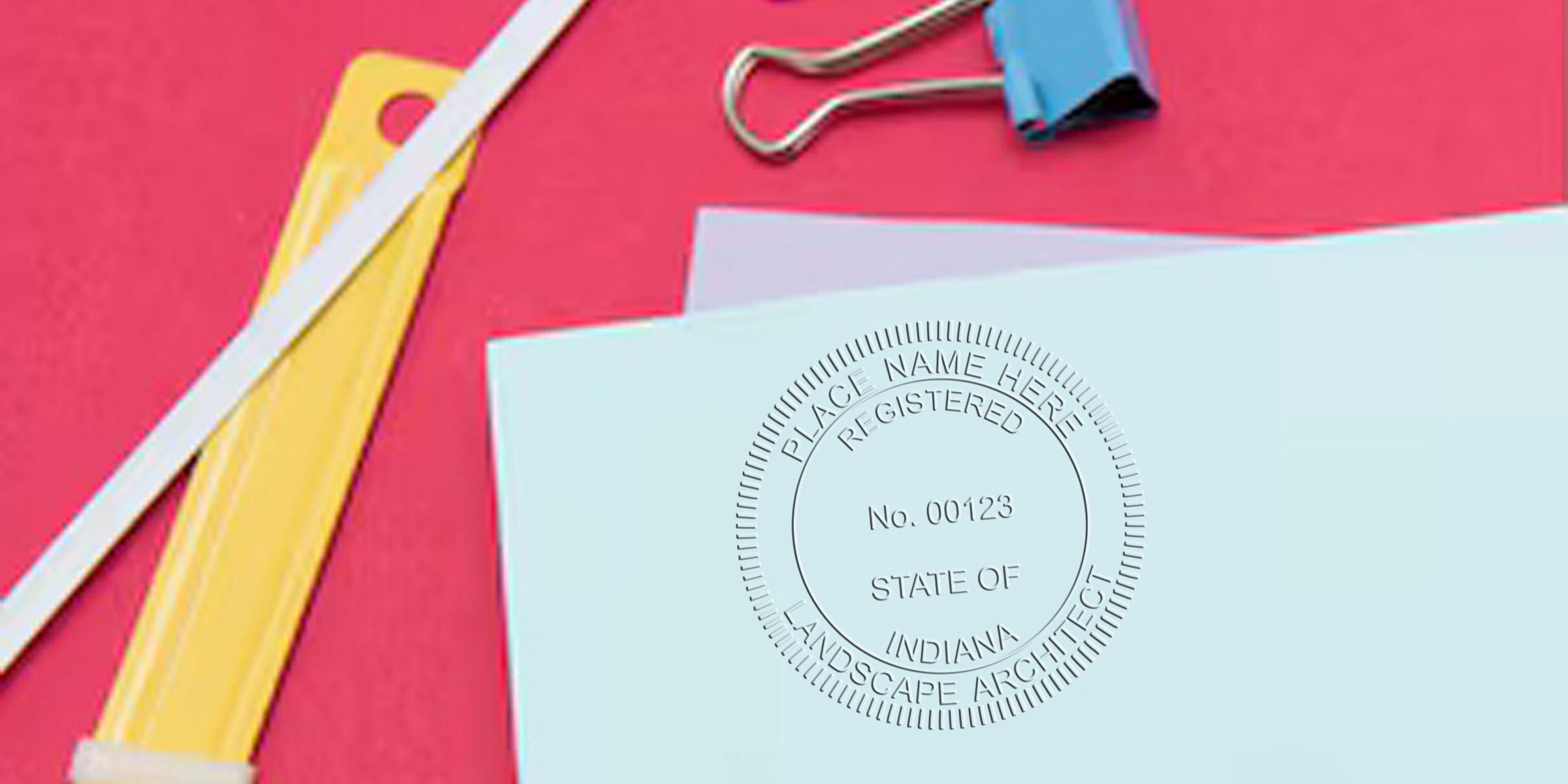 Blue envelope with Indiana landscape architect stamp, yellow letter opener, and blue binder clip on red background, highlighting Indiana landscape architect regulations.
